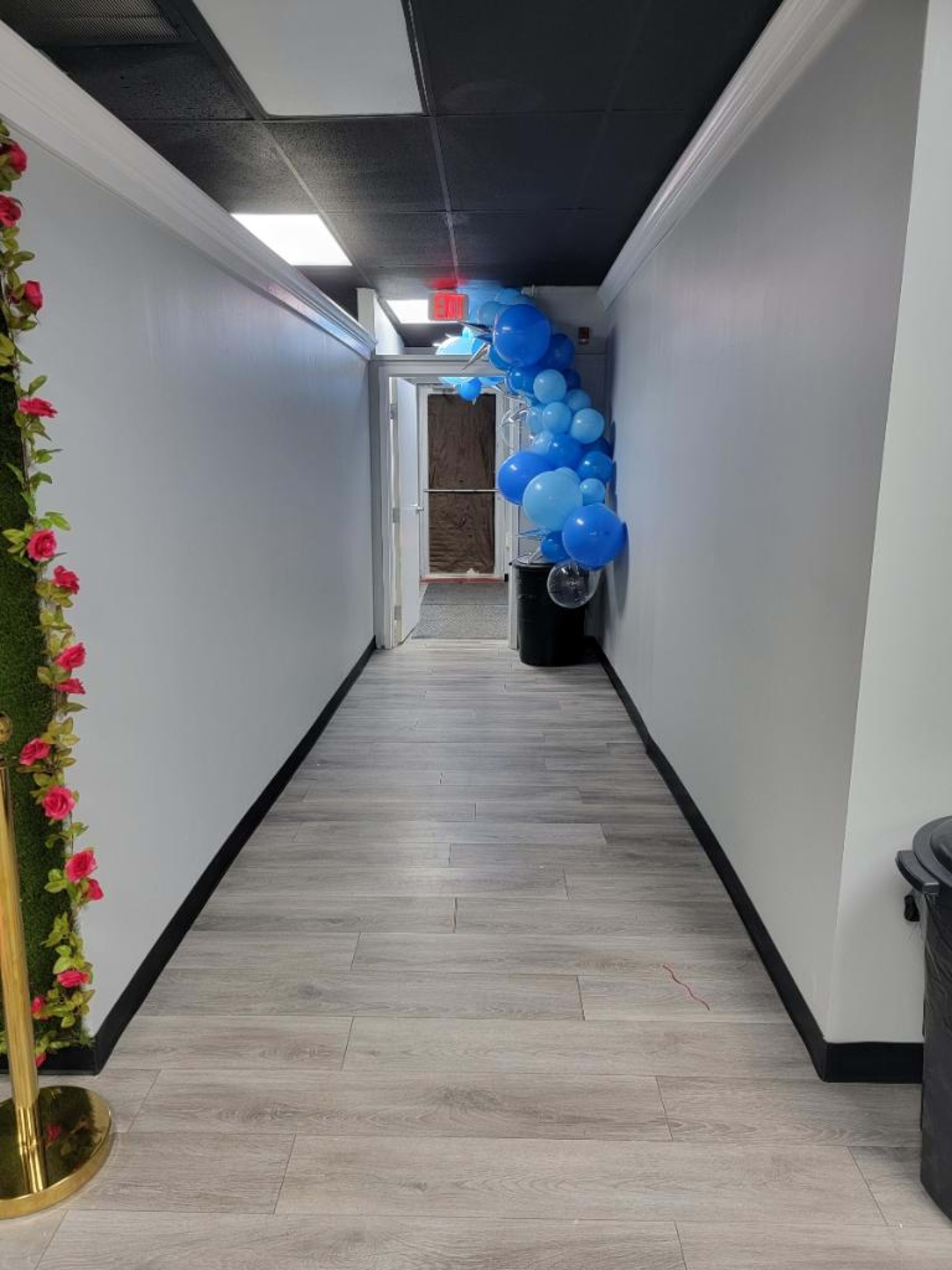 A hallway with light-colored walls features a cluster of blue balloons near an exit door.