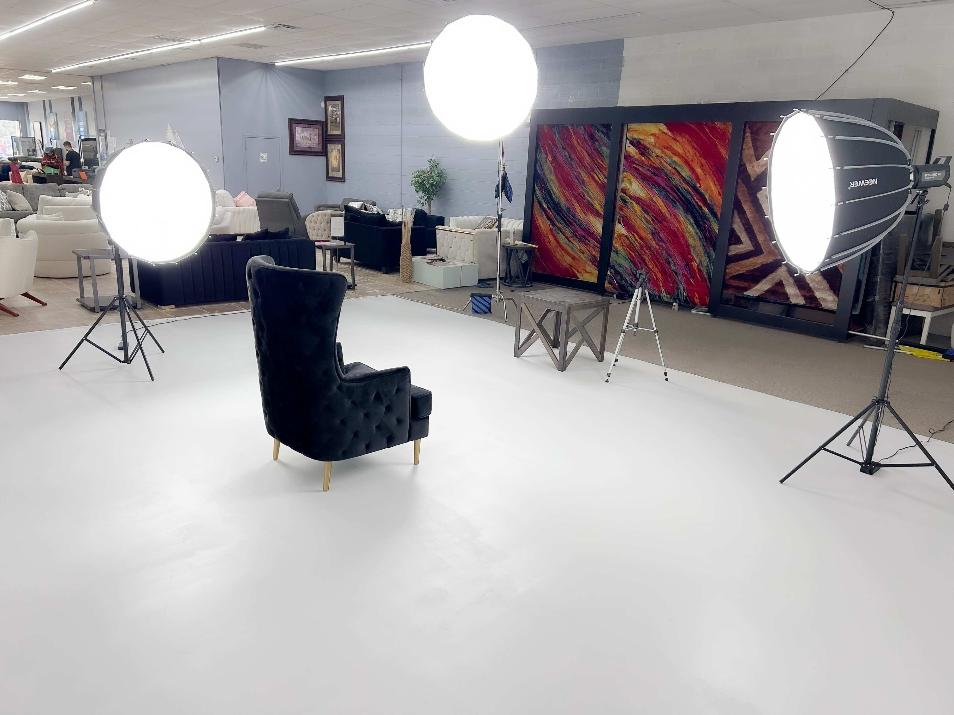 A well-lit studio setup with two large softbox lights, a black tufted chair in the center, and abstract art displayed on the walls.