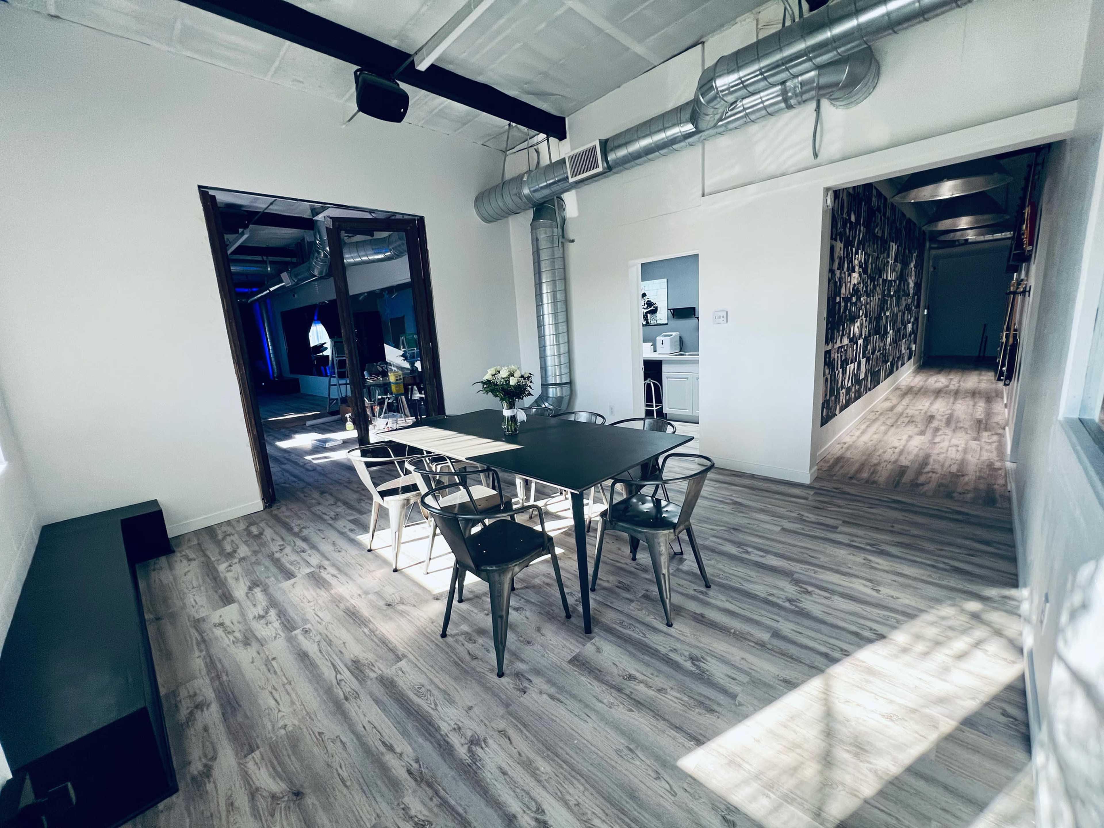 A well-lit, modern interior space featuring a table with chairs, wooden flooring, and an open doorway leading to another area.