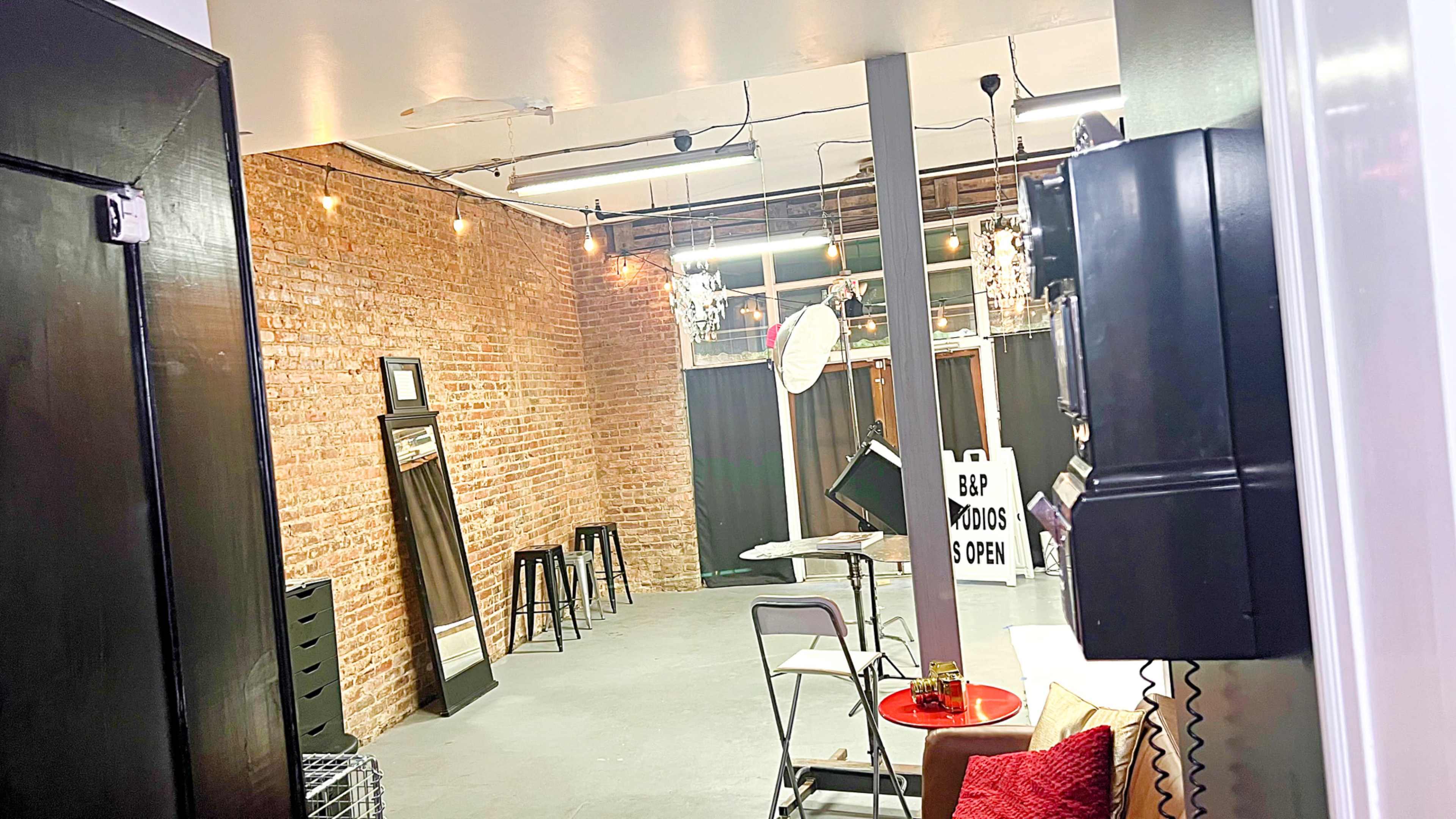 The image shows an industrial-style room with exposed brick walls, a few stools, and various furniture, including a mirror and a sign indicating that food is available.