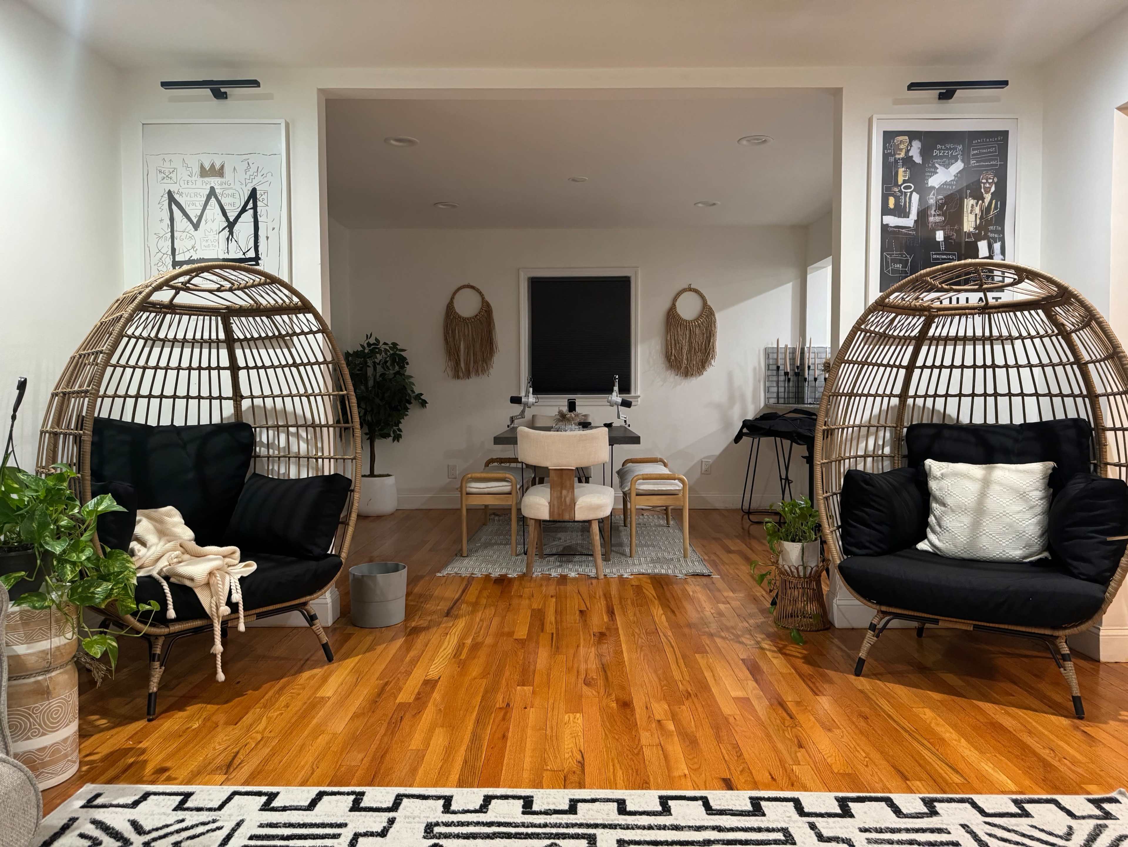 A modern living space featuring two large, rounded wicker chairs on either side, with a dining area and decorative elements in the background.