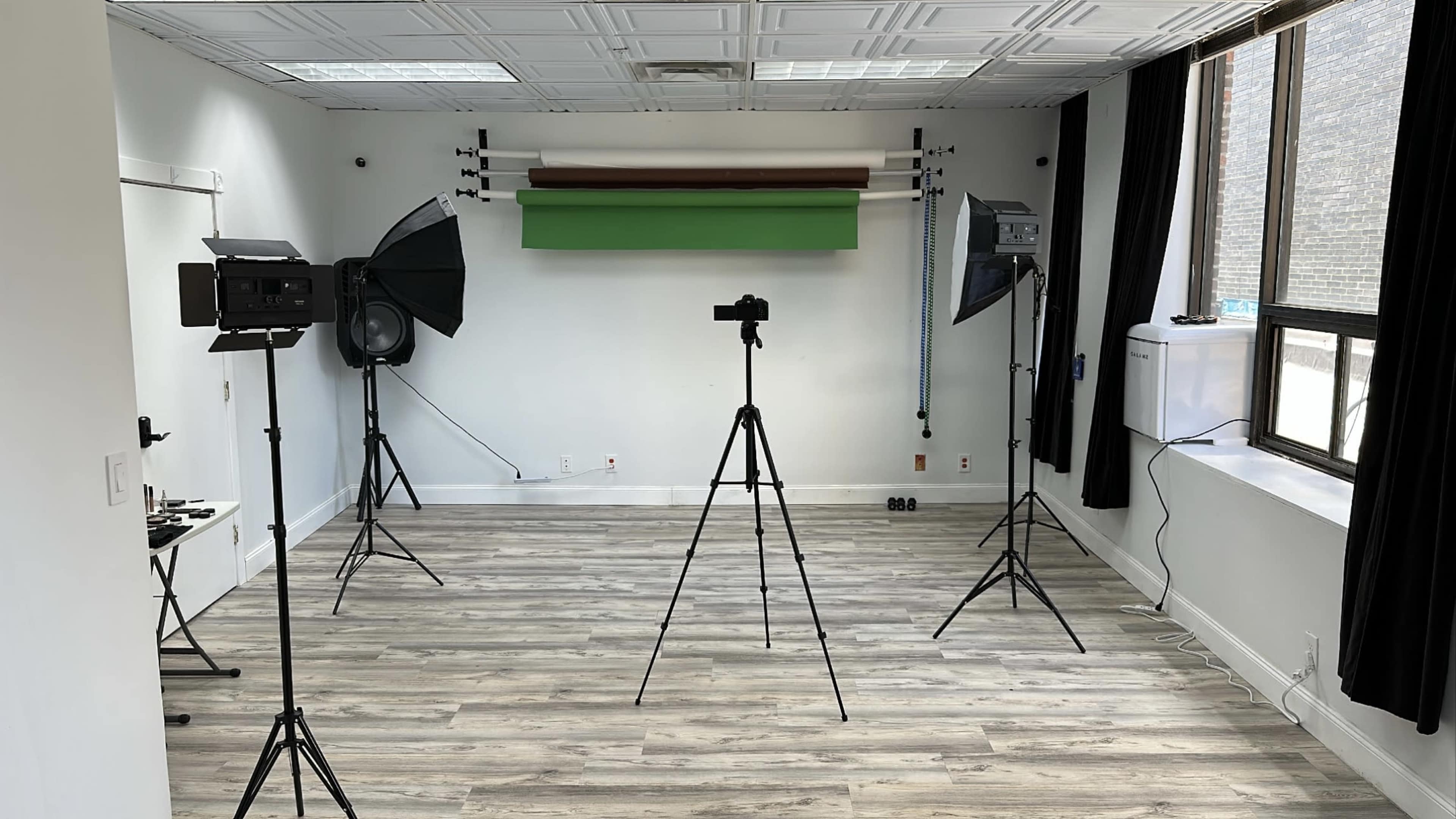 The image shows a photography studio featuring three tripods with cameras, two softbox lights, and a green backdrop.