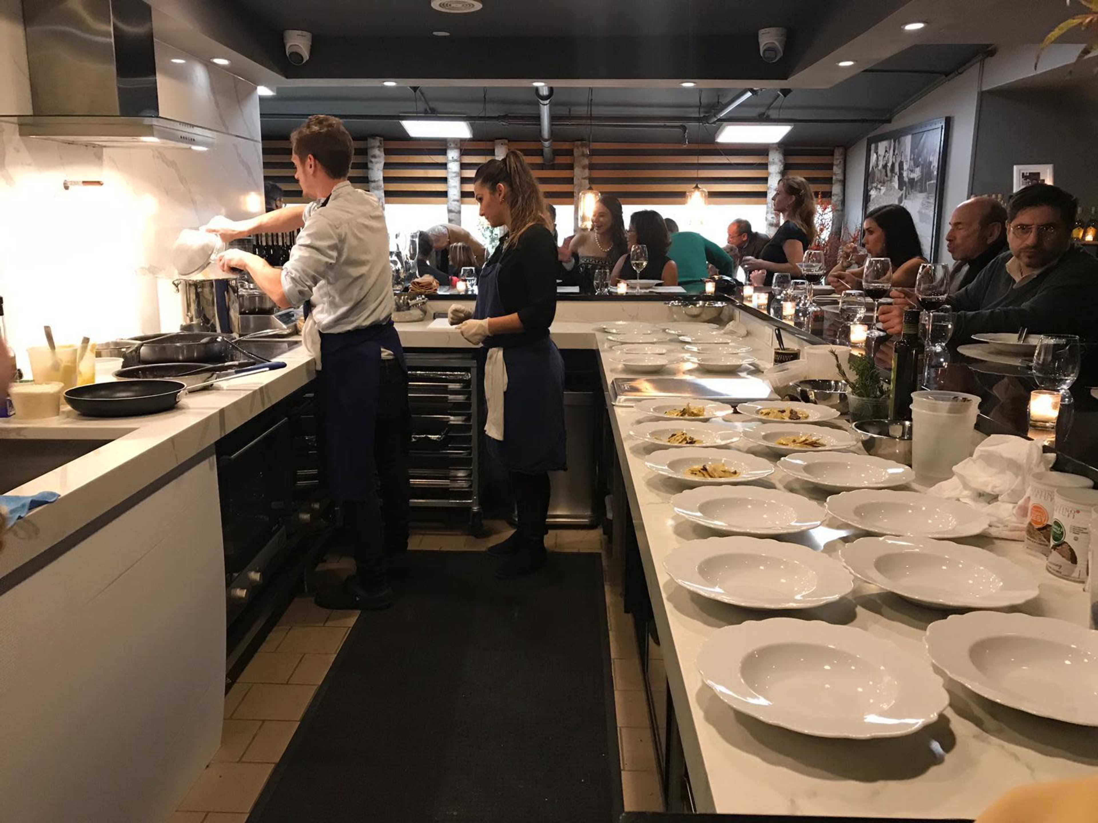 A kitchen filled with chefs preparing dishes while diners enjoy their meals at a communal dining setup.