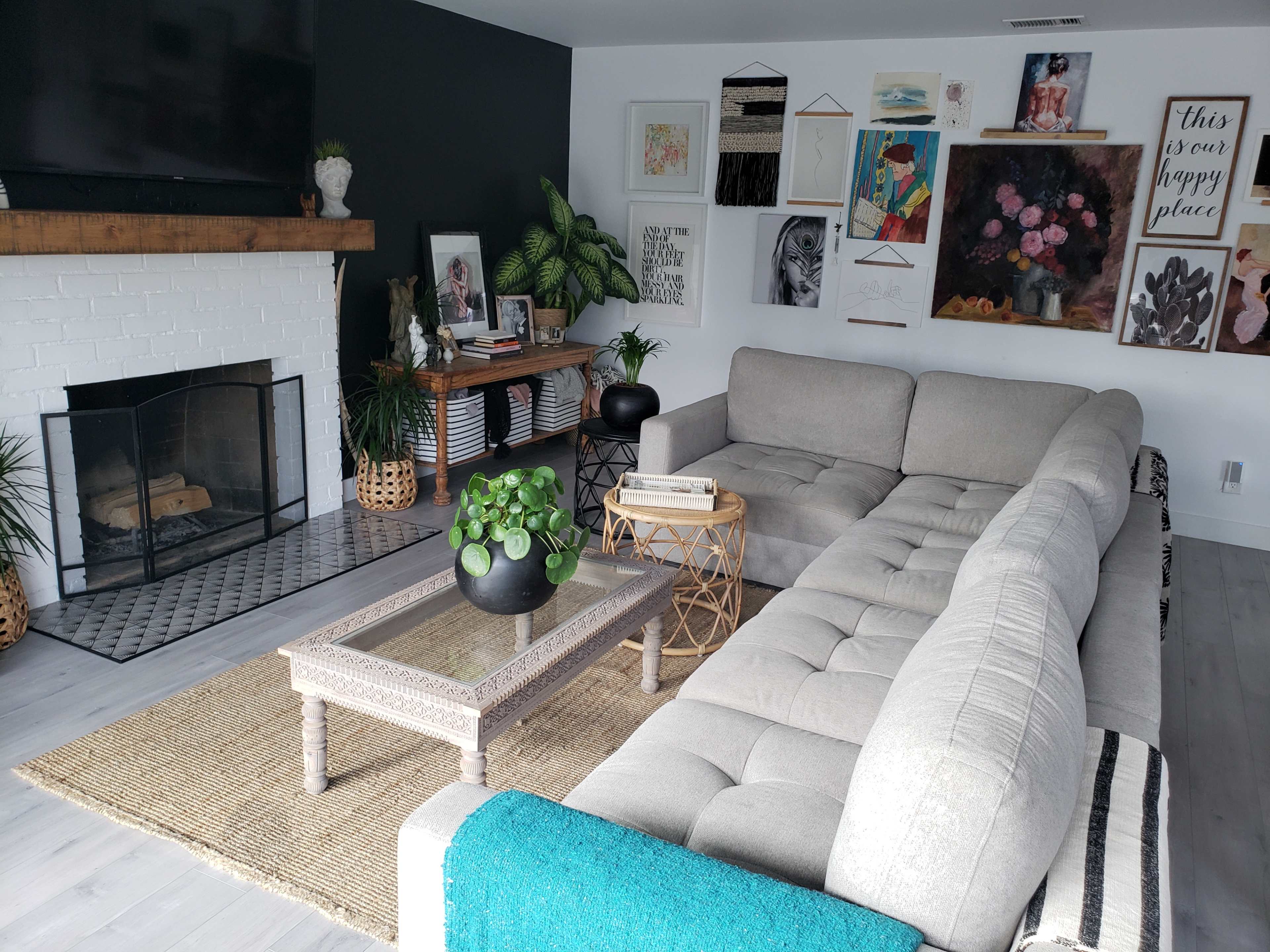 The living room features a large sectional sofa, a coffee table, and a fireplace, surrounded by decorative artwork and houseplants.