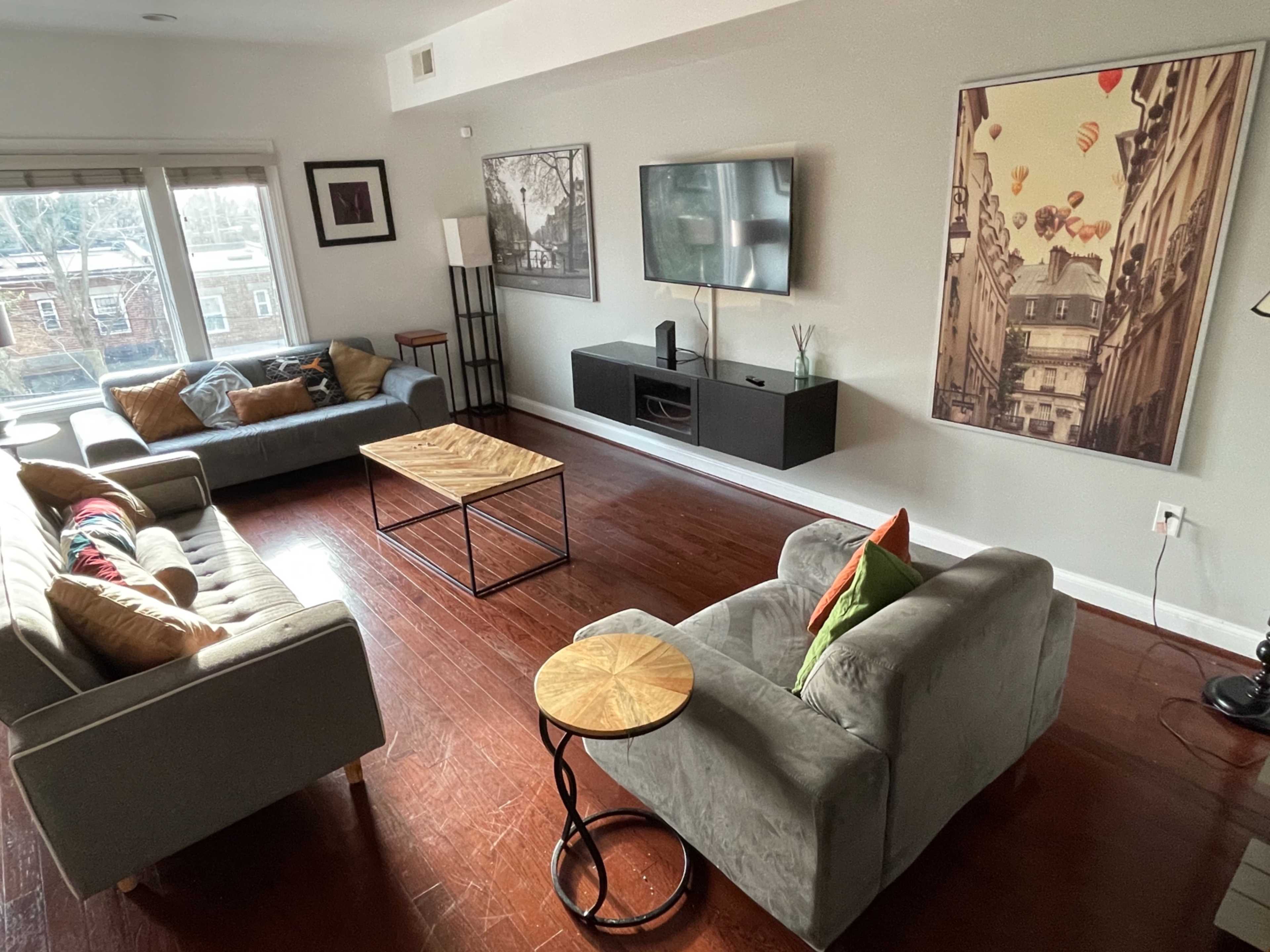 A living room with two sofas, an armchair, a coffee table, and framed artwork on the walls, all arranged around a television mounted on a console.