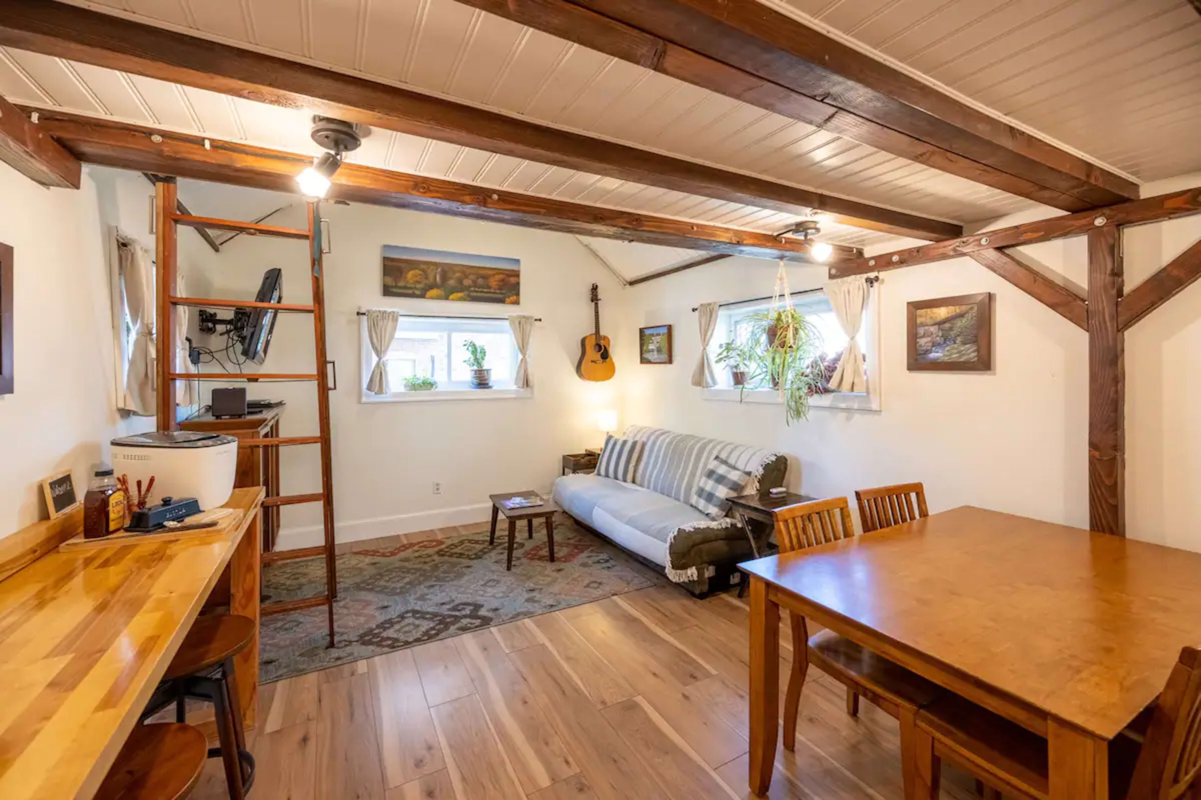 A cozy indoor living space featuring a sofa, wooden dining table, and exposed beams along the ceiling.