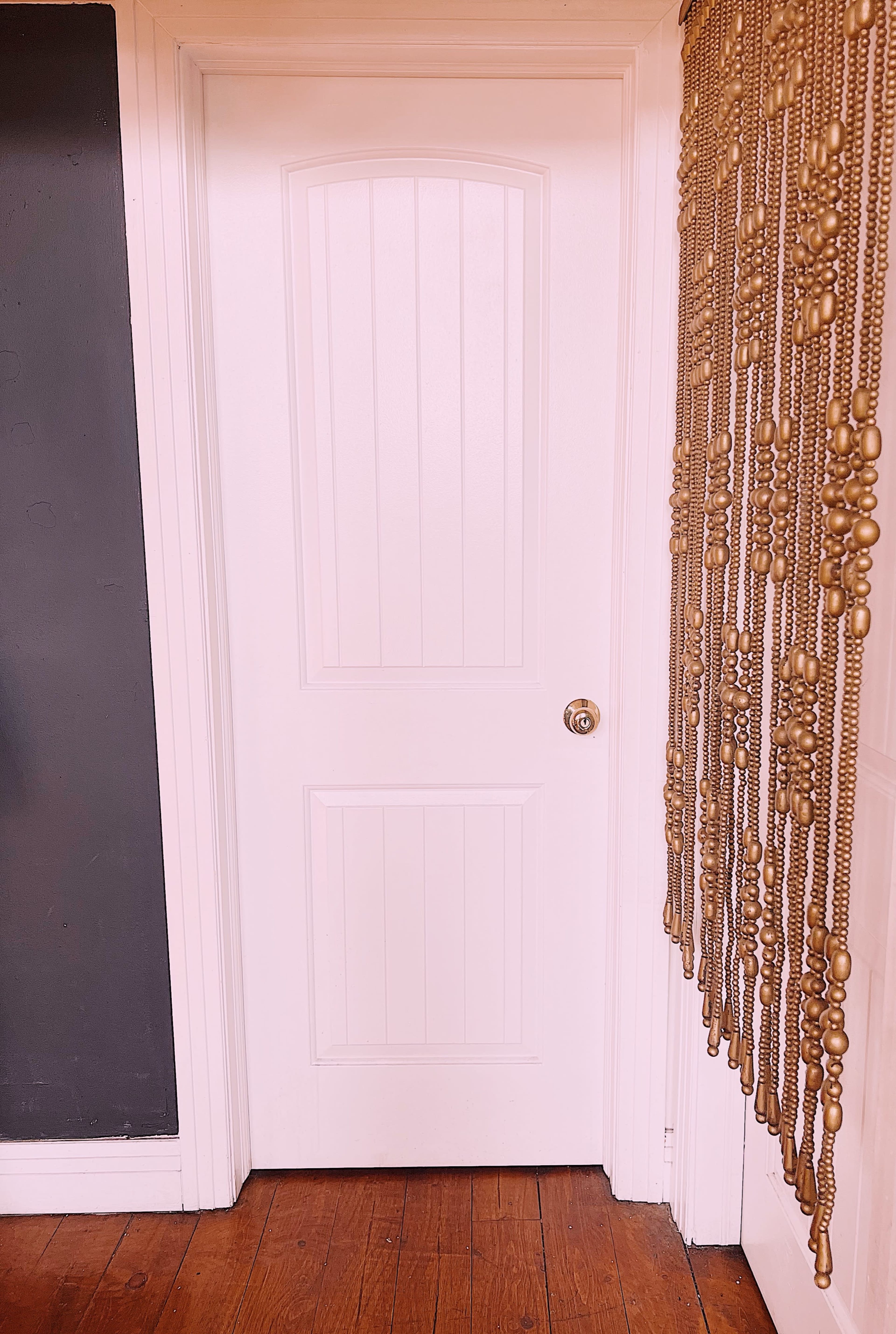 A white paneled door next to a wall decorated with a curtain made of golden beads.