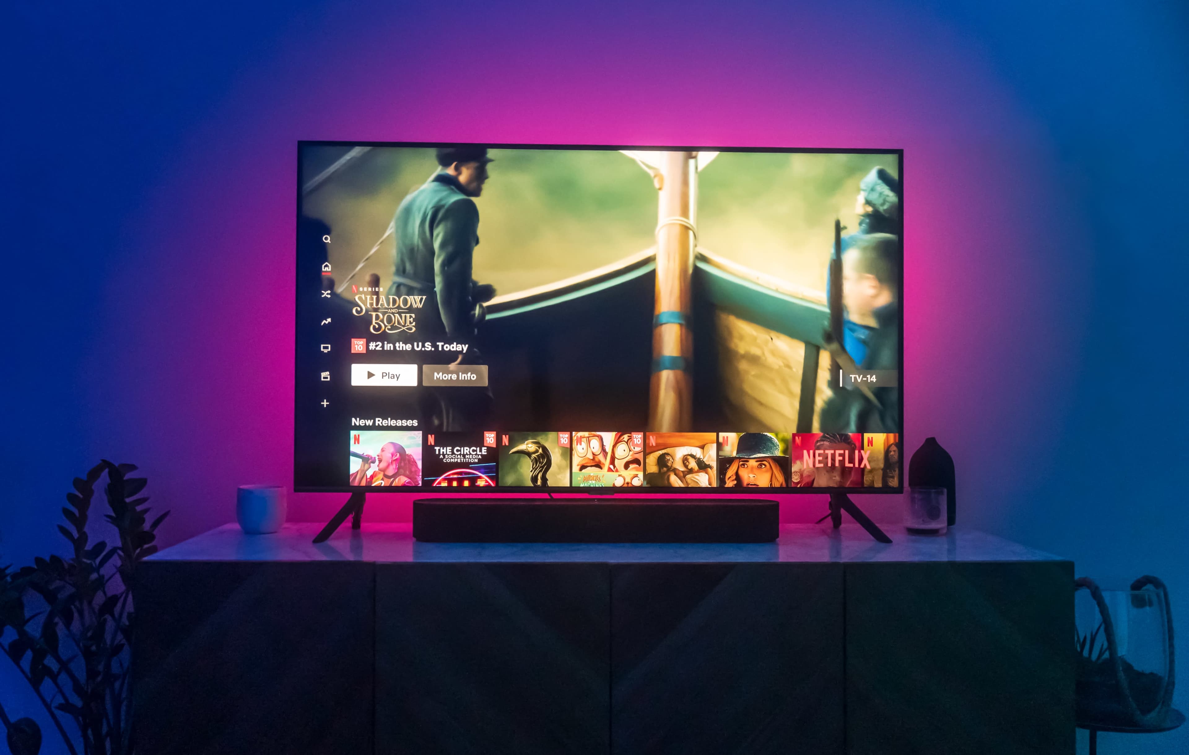 A television displaying a streaming service interface is set on a low cabinet with ambient lighting behind it.