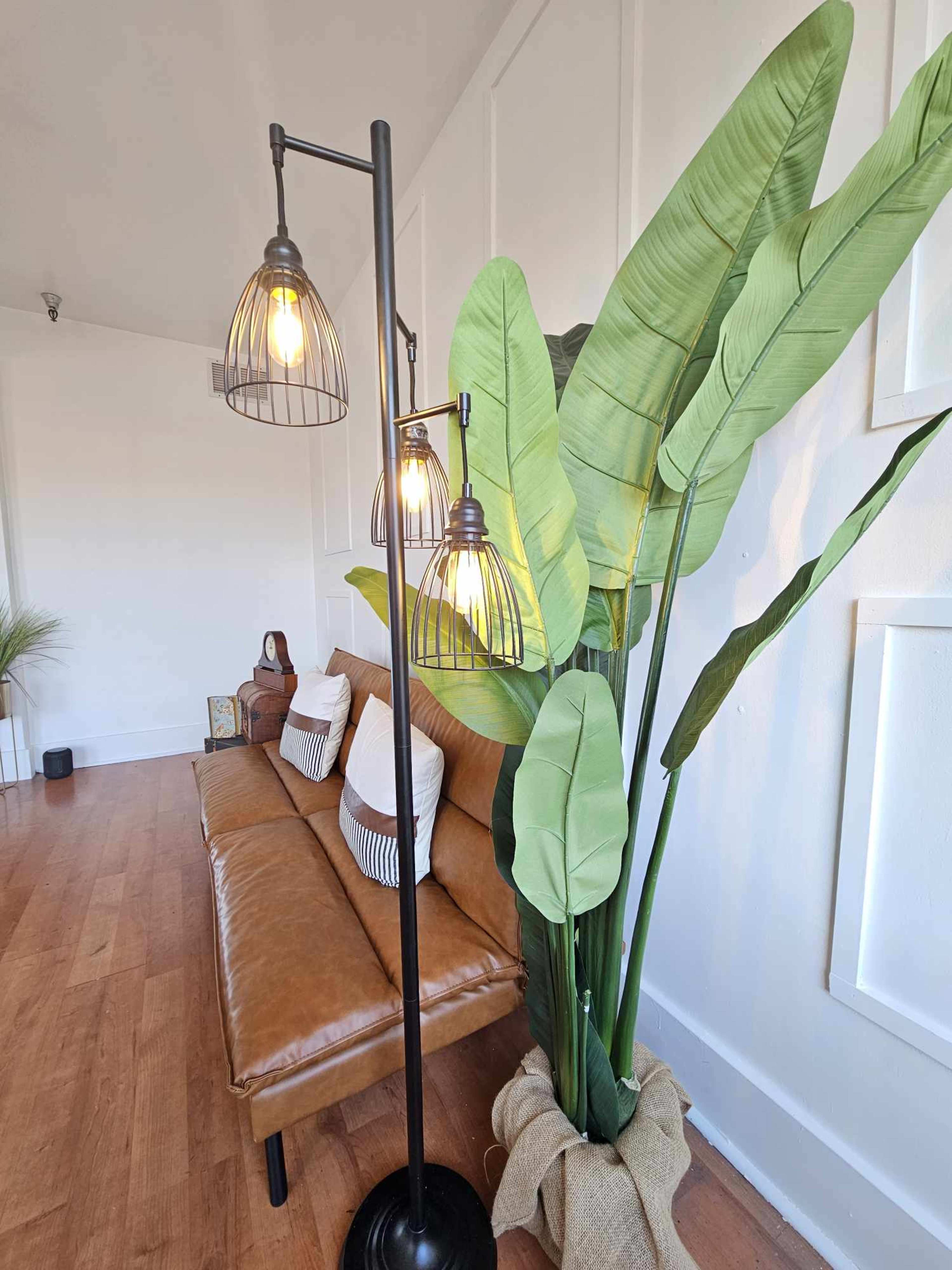 A modern living room with a brown leather sofa, three pendant lights, and a tall potted plant beside it.