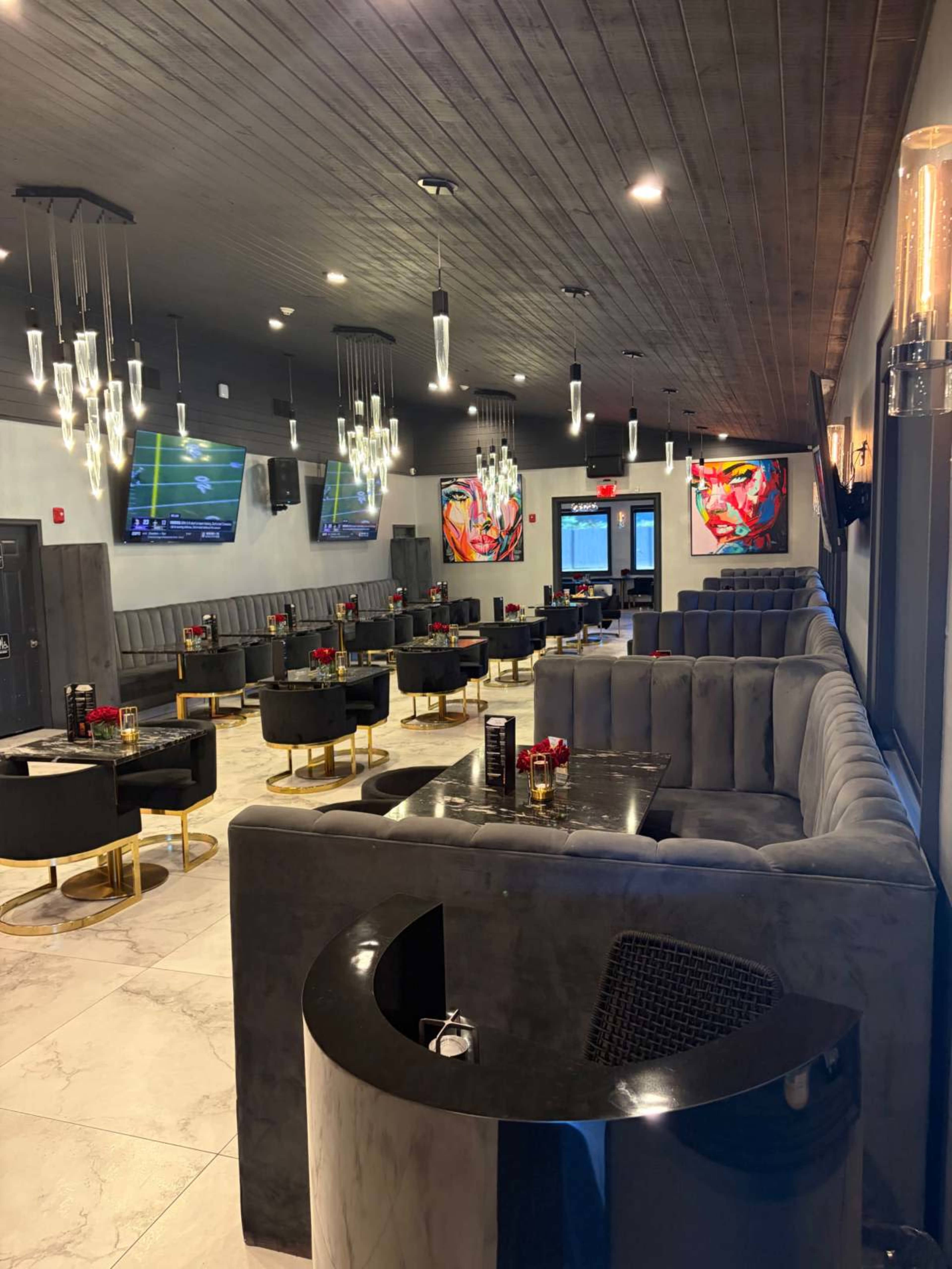 The image shows a modern restaurant interior featuring plush gray seating, marble flooring, and multiple flat-screen TVs mounted on the walls.