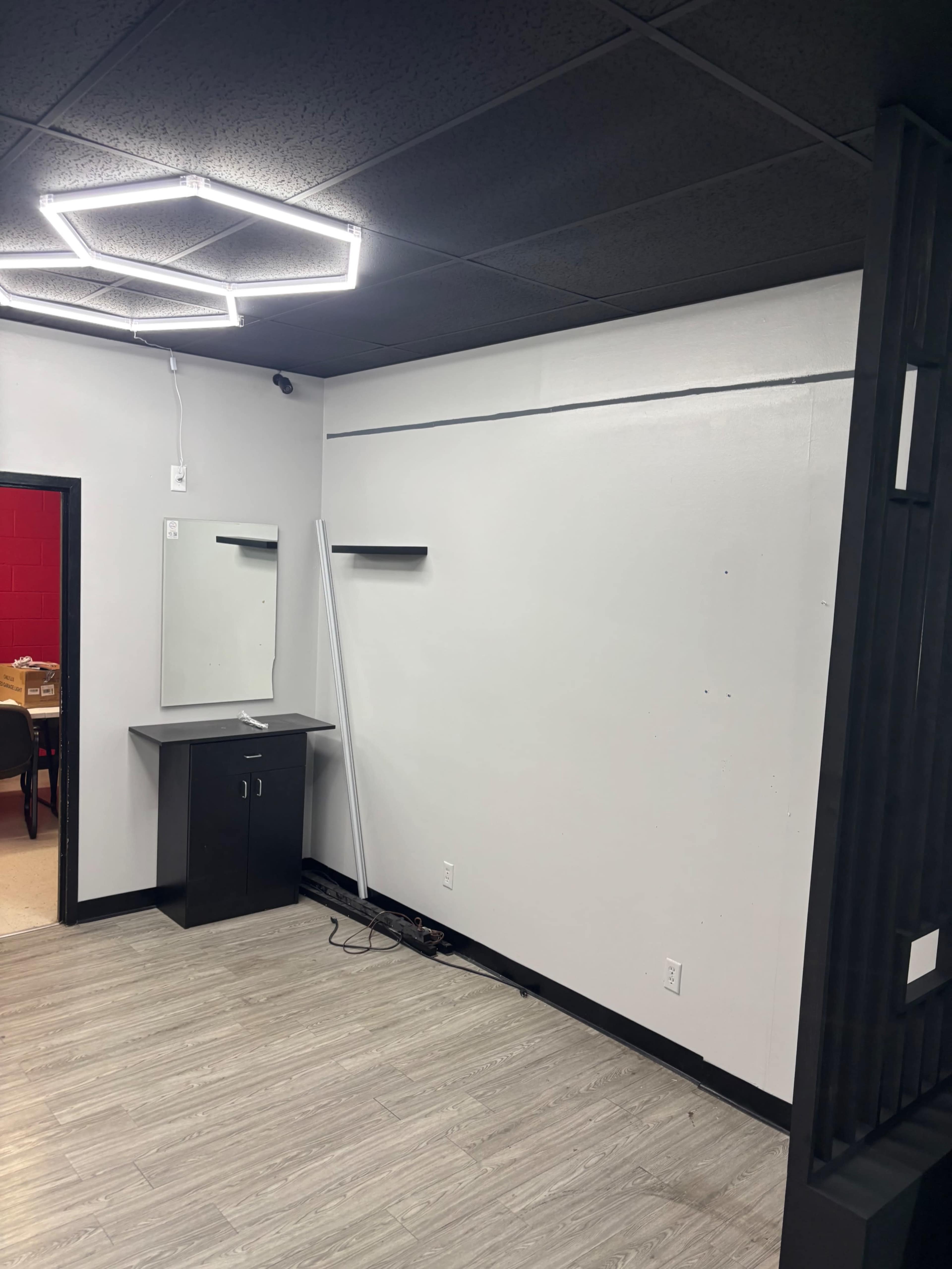 The image shows an empty room with a lighted ceiling fixture, a vanity against one wall, and a bare wall beside it.