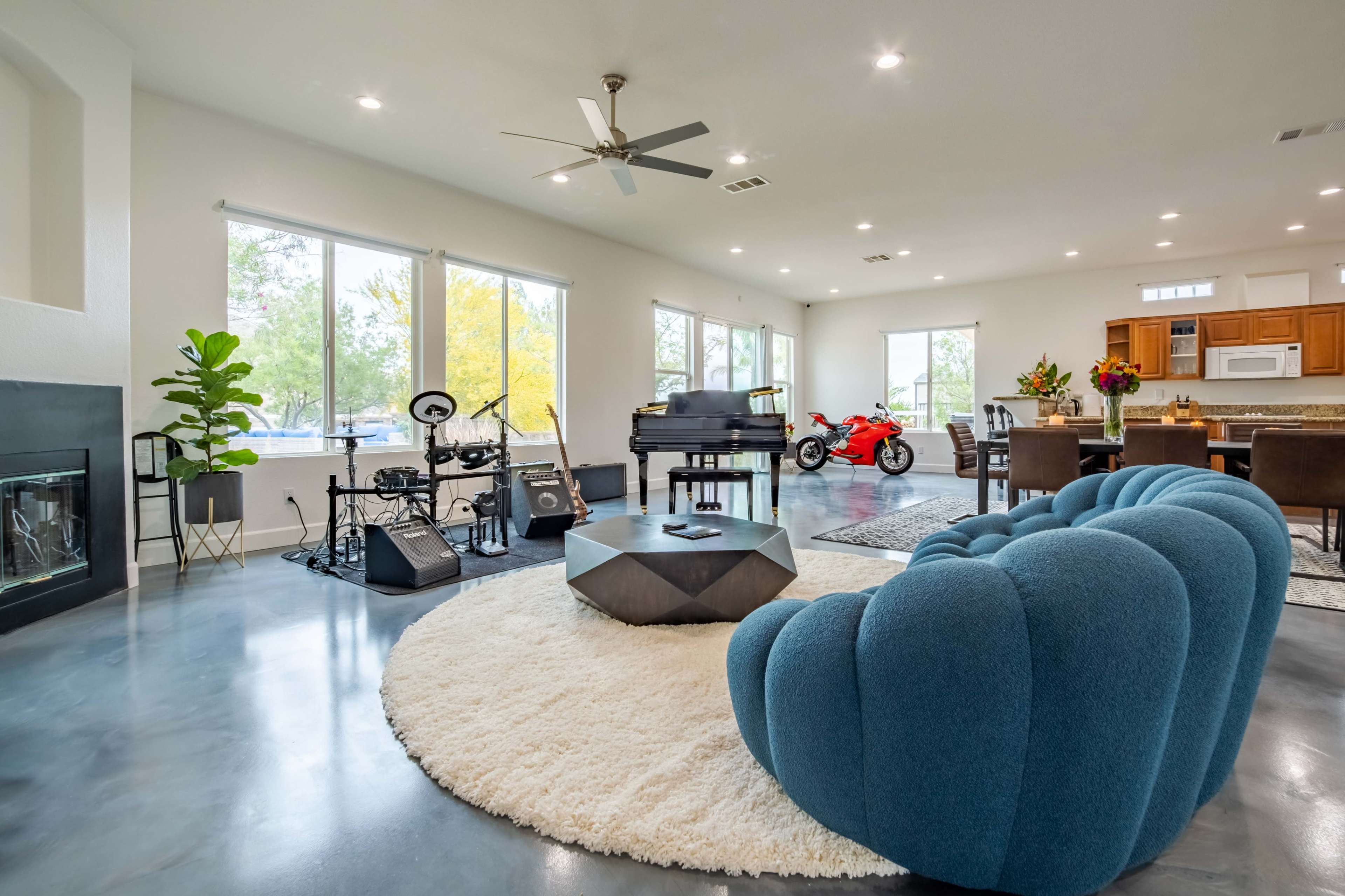 A spacious living room features a blue sofa, a drum set, a black piano, a red motorcycle, and a dining area with a large table.