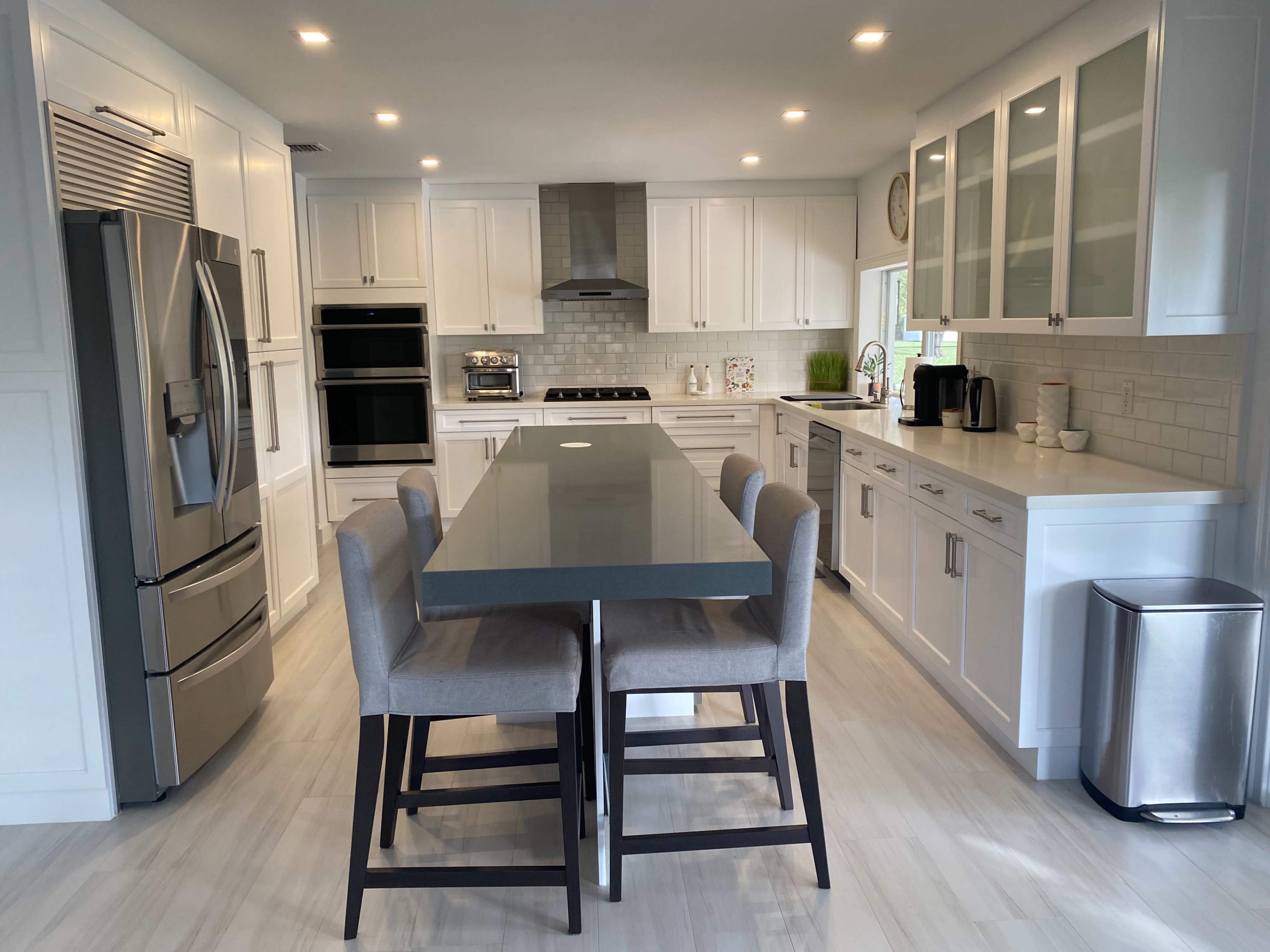A modern kitchen featuring white cabinetry, stainless steel appliances, and a long island with seating for four.