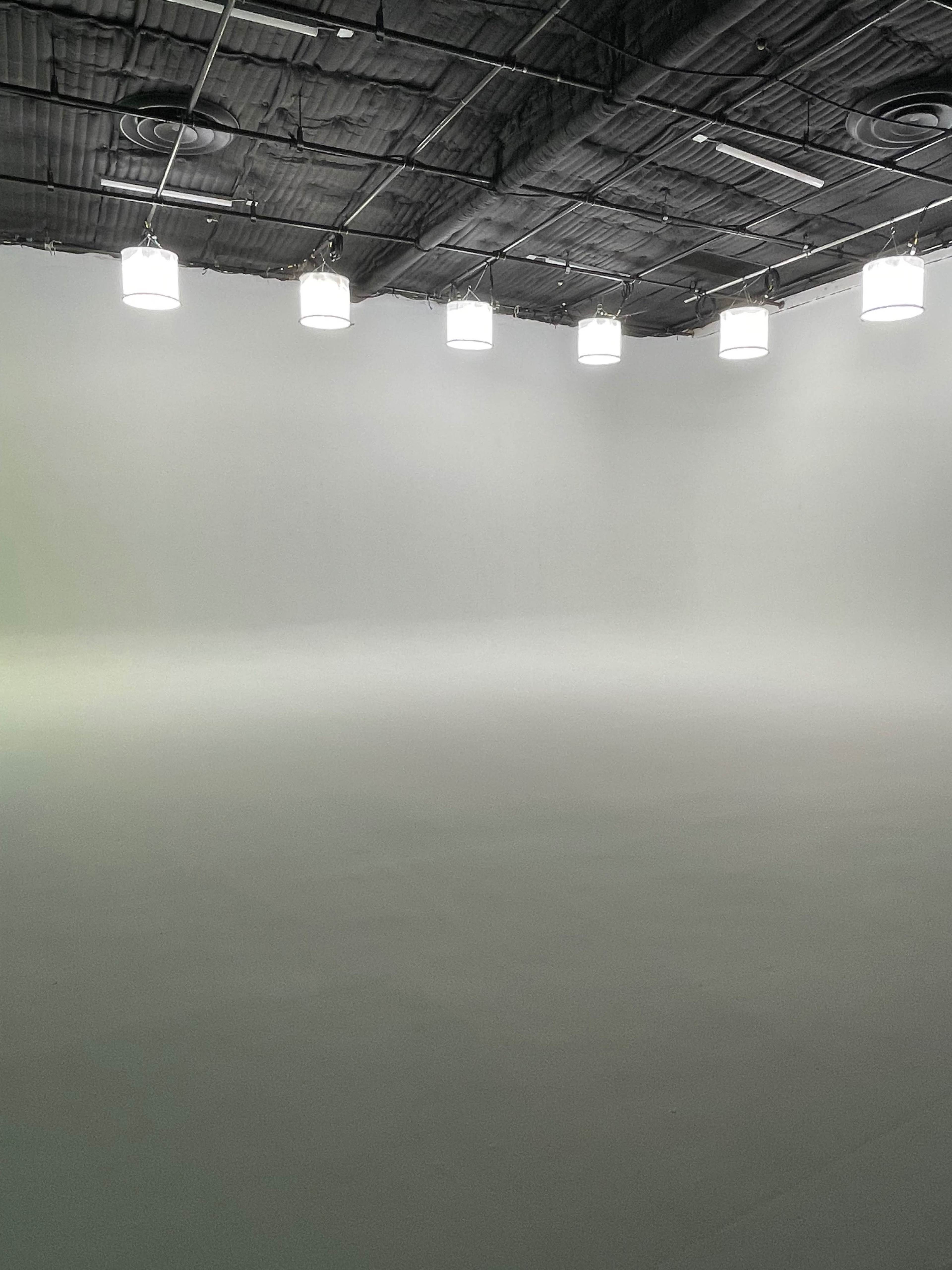 A large, empty studio with a smooth white floor and ceiling lights hanging above.