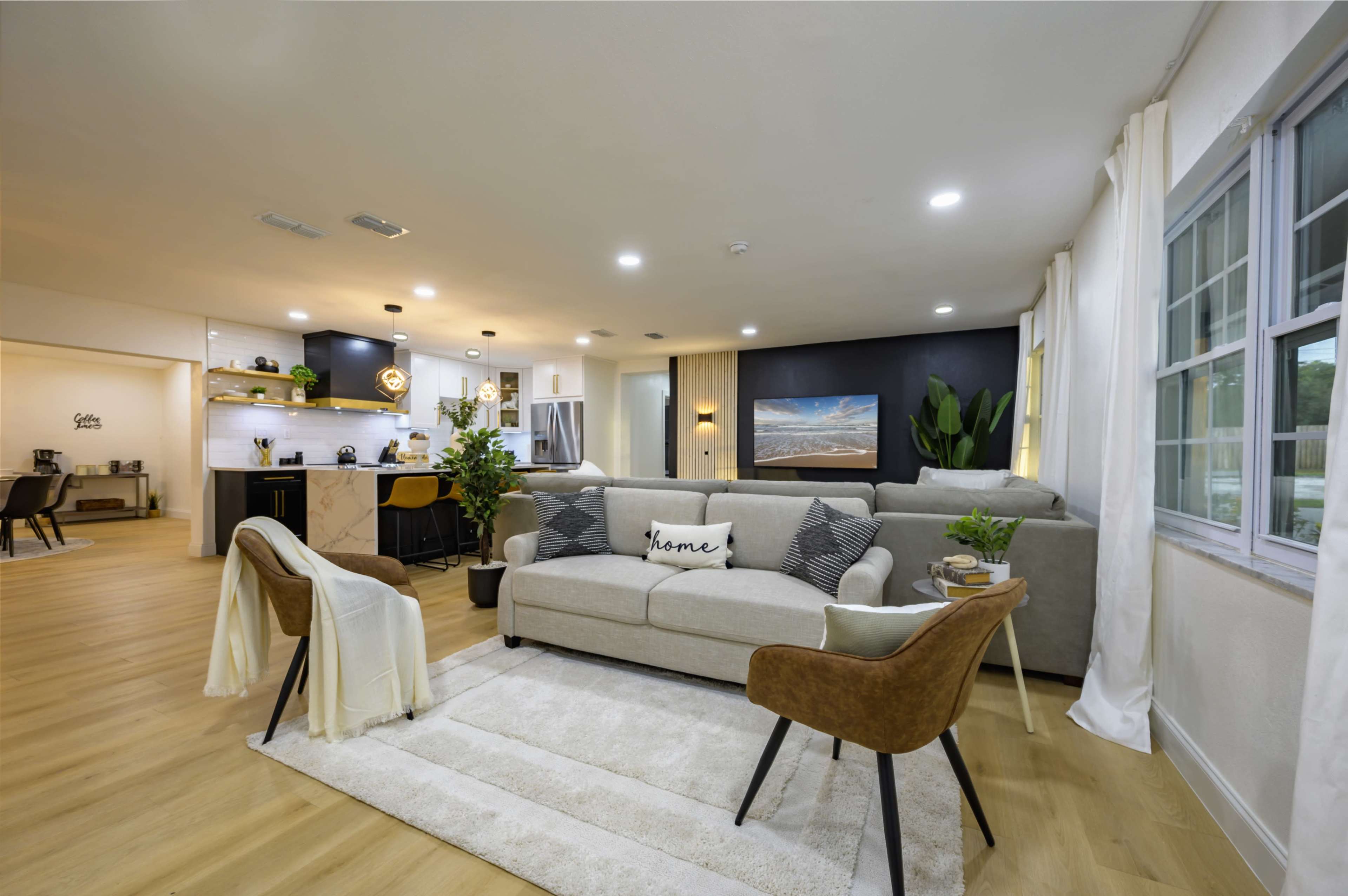 A modern living room with a light-colored sofa, two brown chairs, and a large window, all set against a mix of light and dark walls.