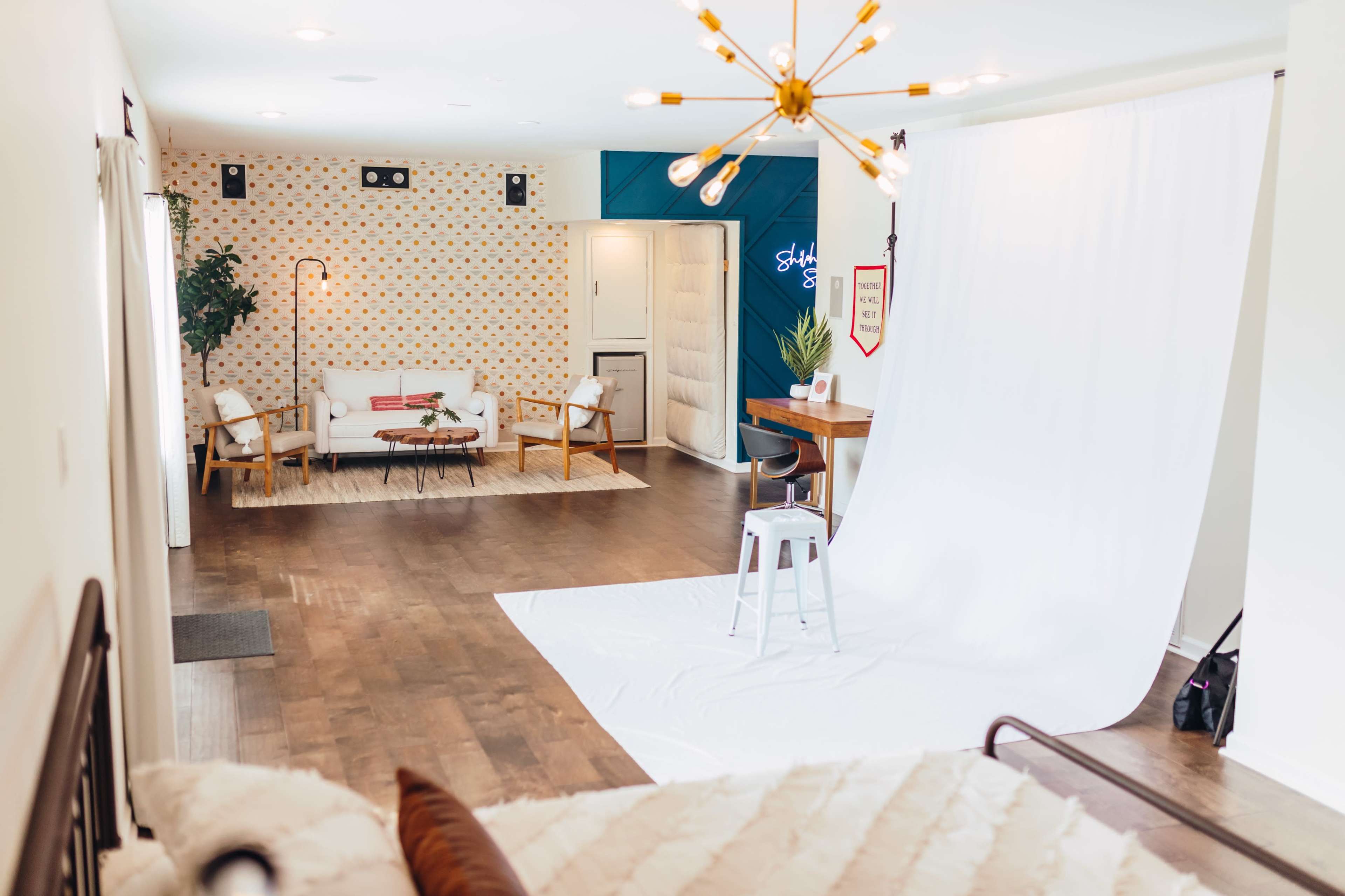 The image shows a spacious, well-lit room with a seating area and a white backdrop for photography.
