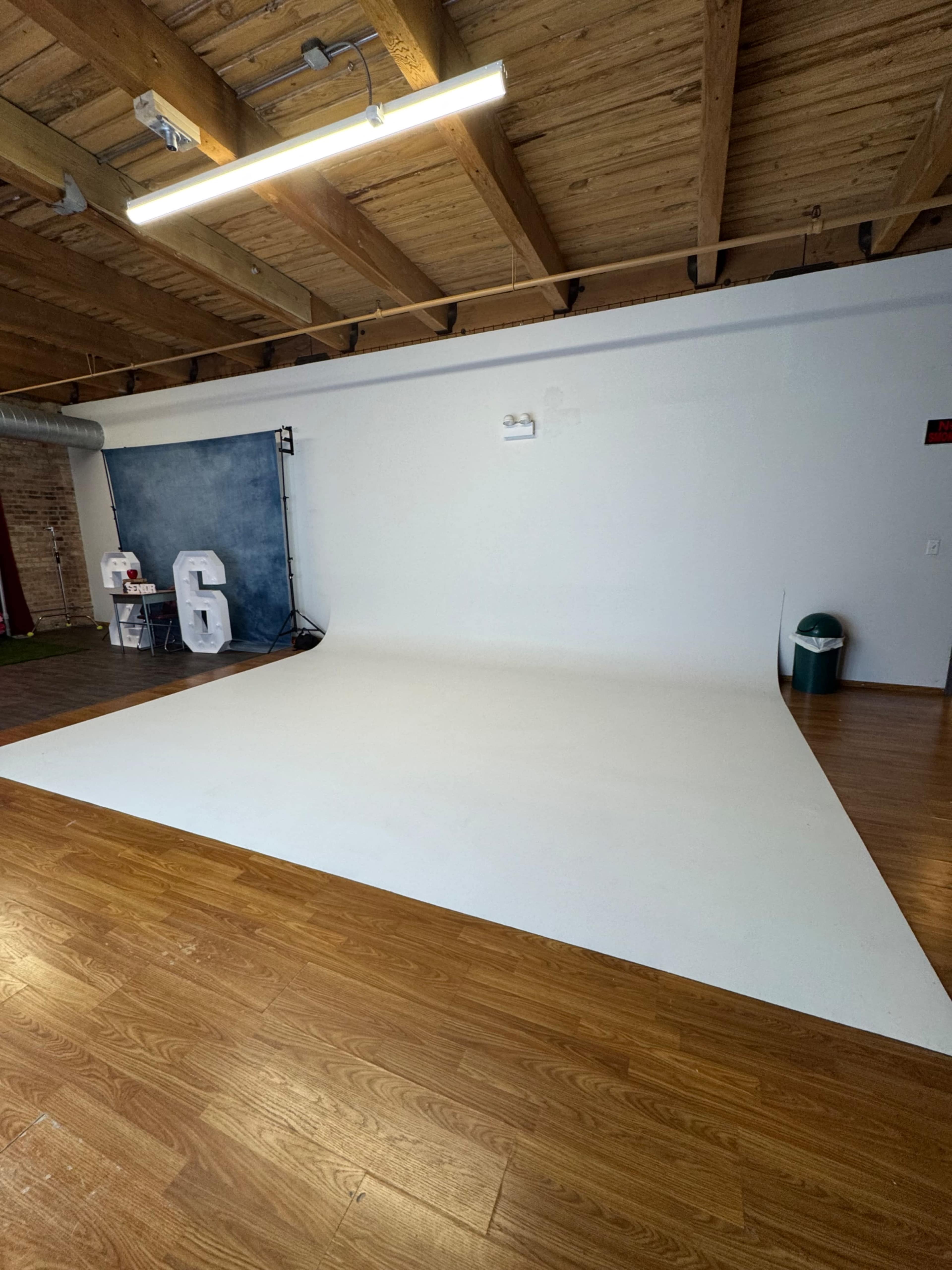 The image shows a spacious photography studio with a white backdrop, wooden floors, and minimal decor.
