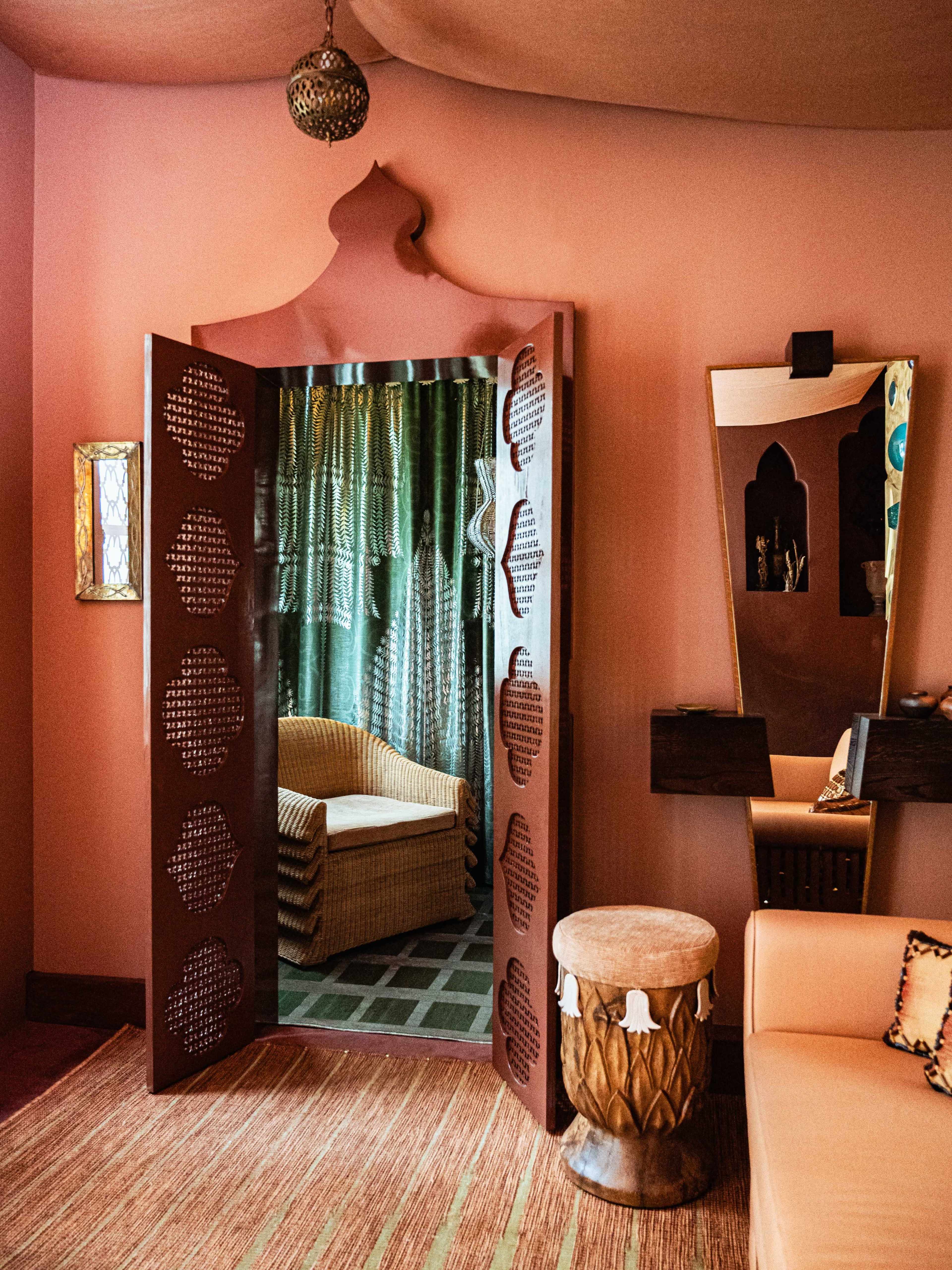 The image shows a decorative interior room featuring intricate wooden doors, a mirror, a seating area, and a drum.