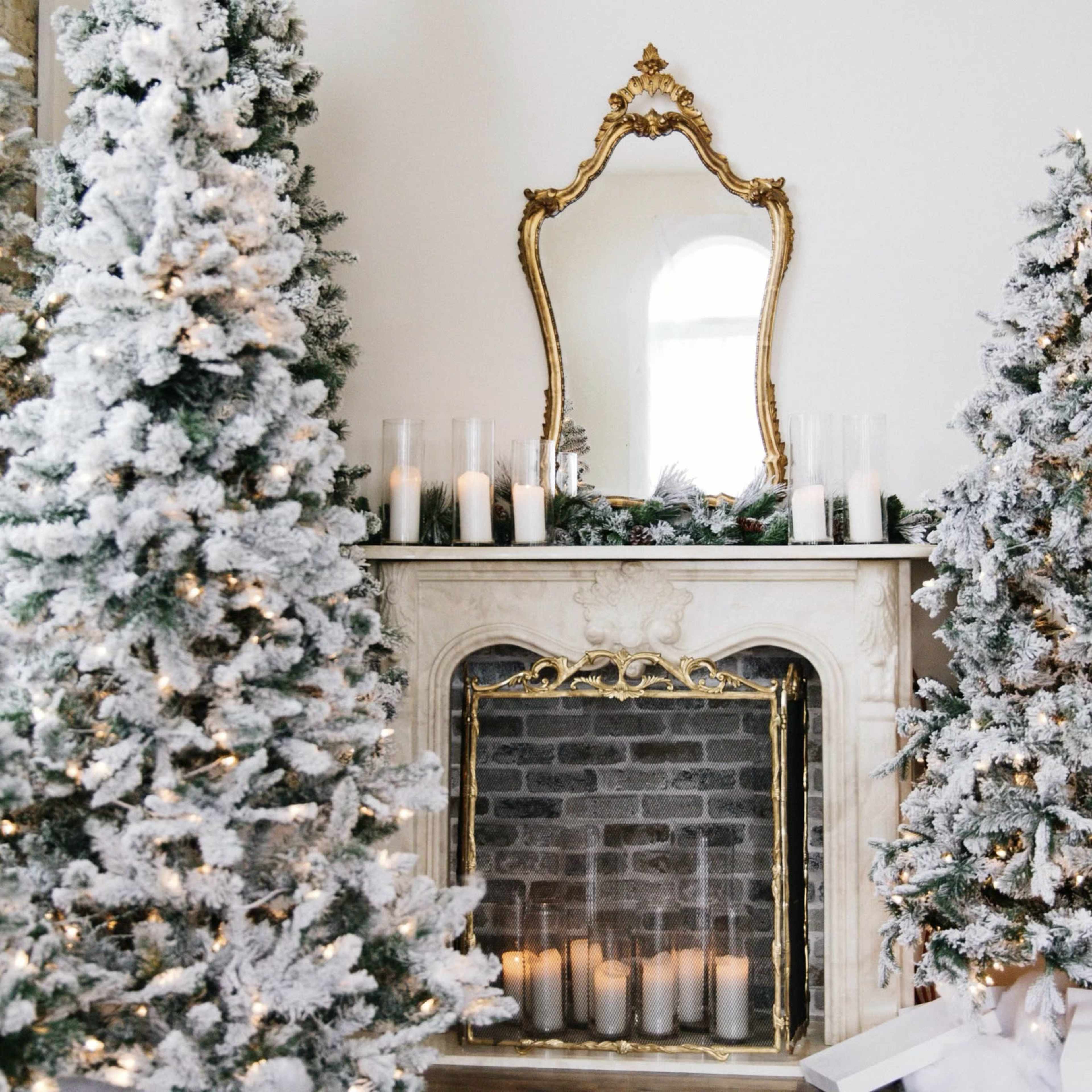 The image shows a decorated fireplace flanked by two snowy Christmas trees, with candles arranged on the mantle and a large mirror above.