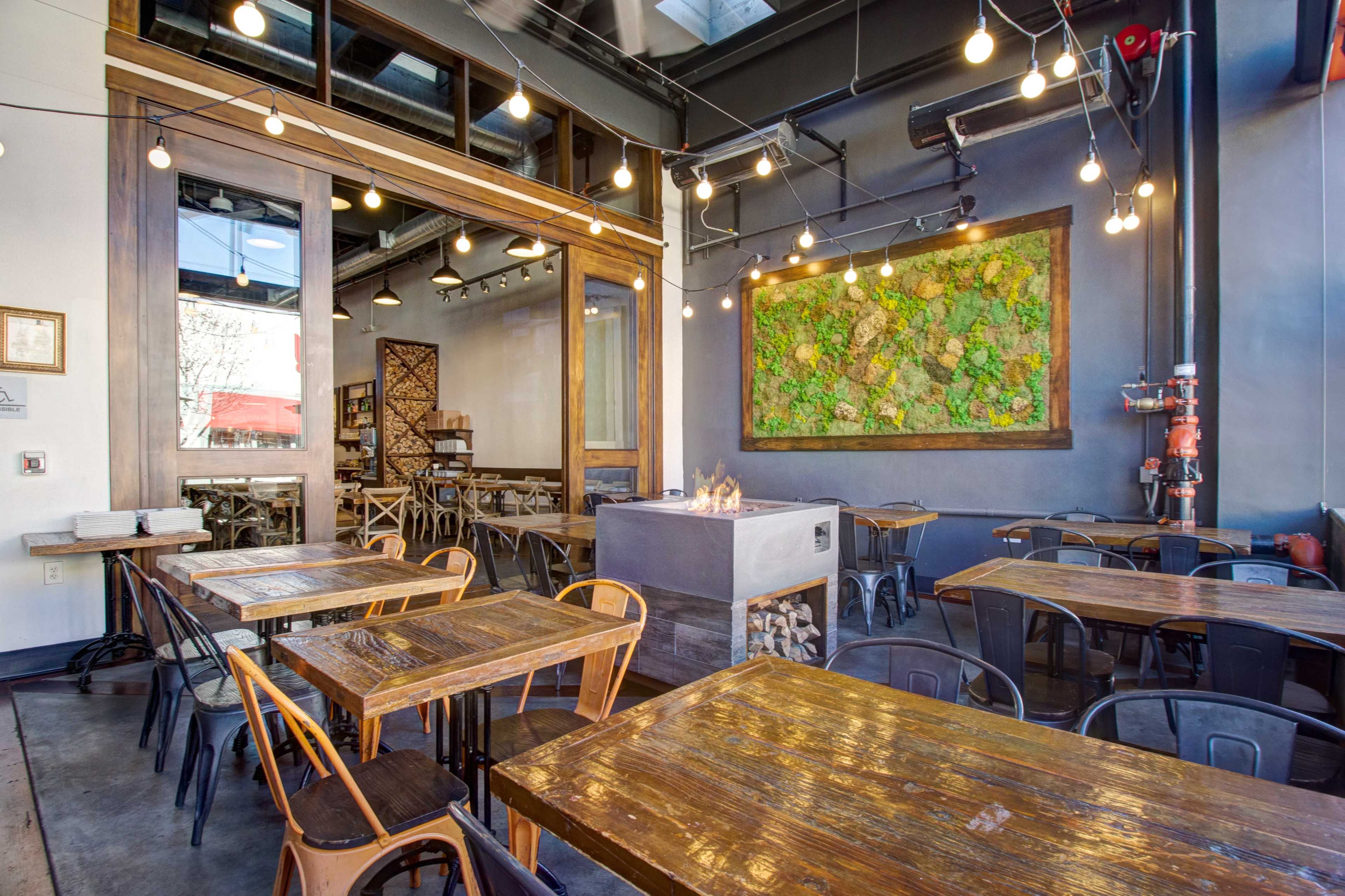 A modern restaurant interior featuring wooden tables, industrial-style chairs, and a decorative moss wall with ambient lighting.