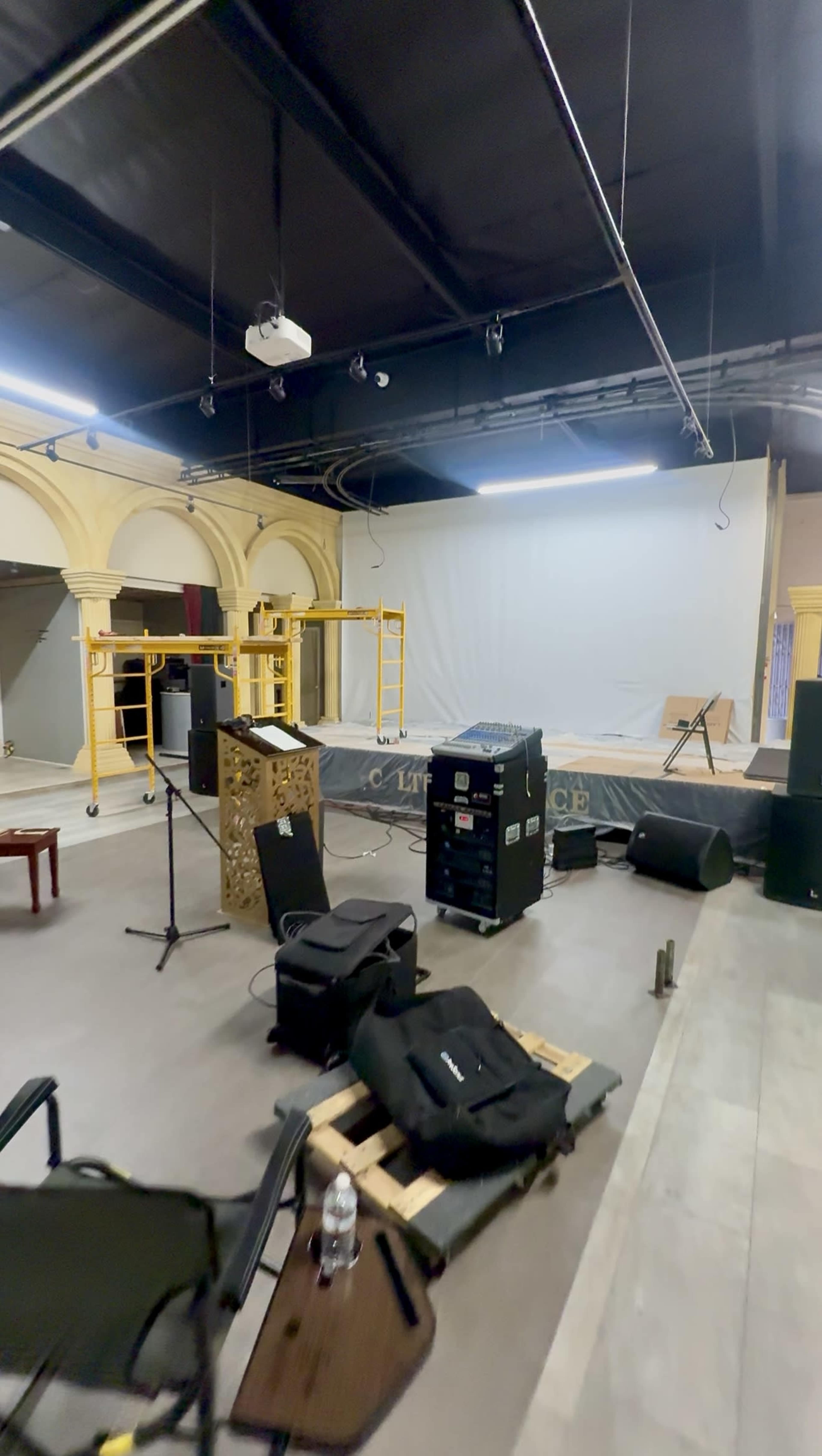 The image shows an empty performance space with equipment like speakers, a microphone stand, and staging materials scattered around.