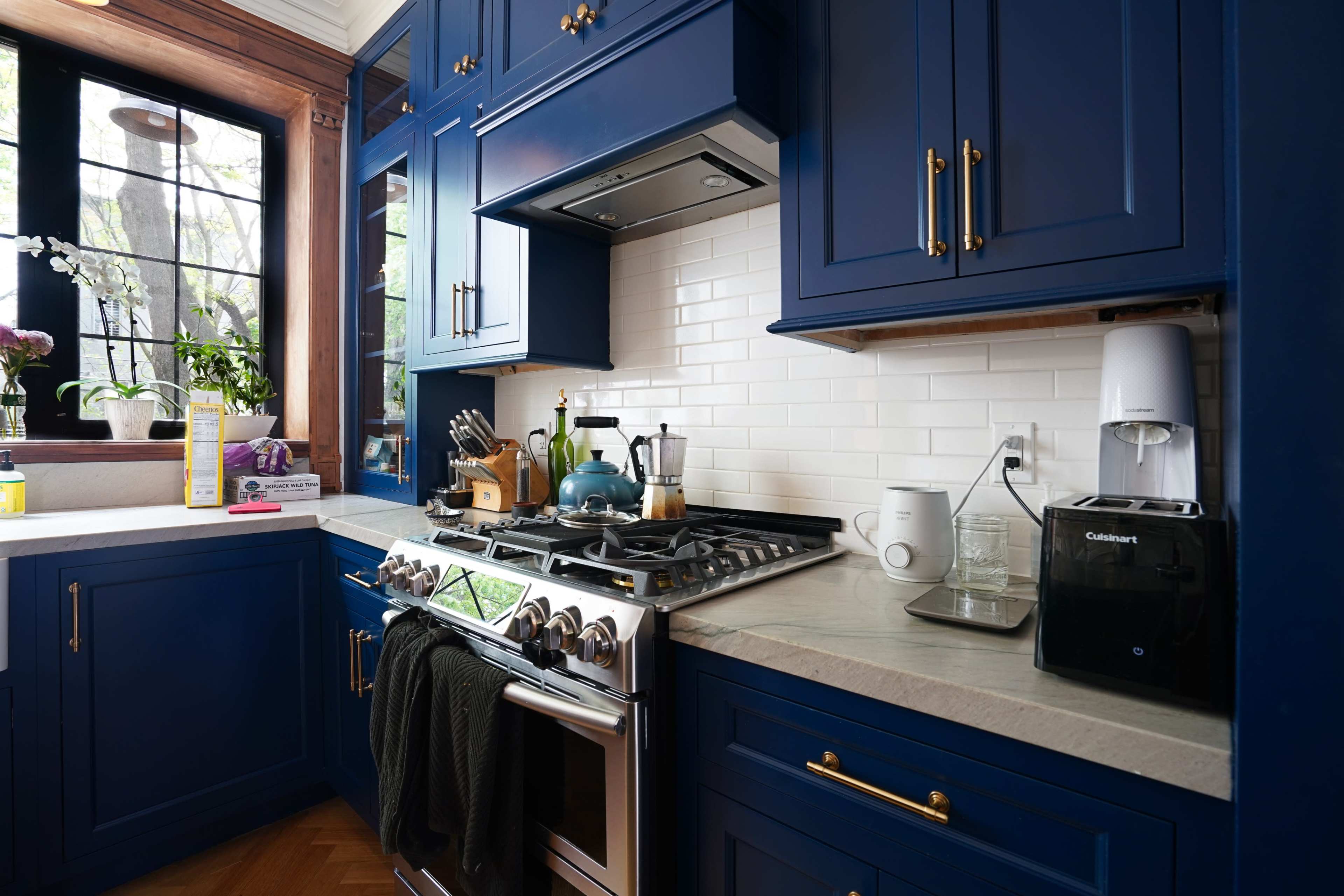 The image features a kitchen with blue cabinetry, a stainless steel stove, and a countertop with various kitchen appliances and utensils.