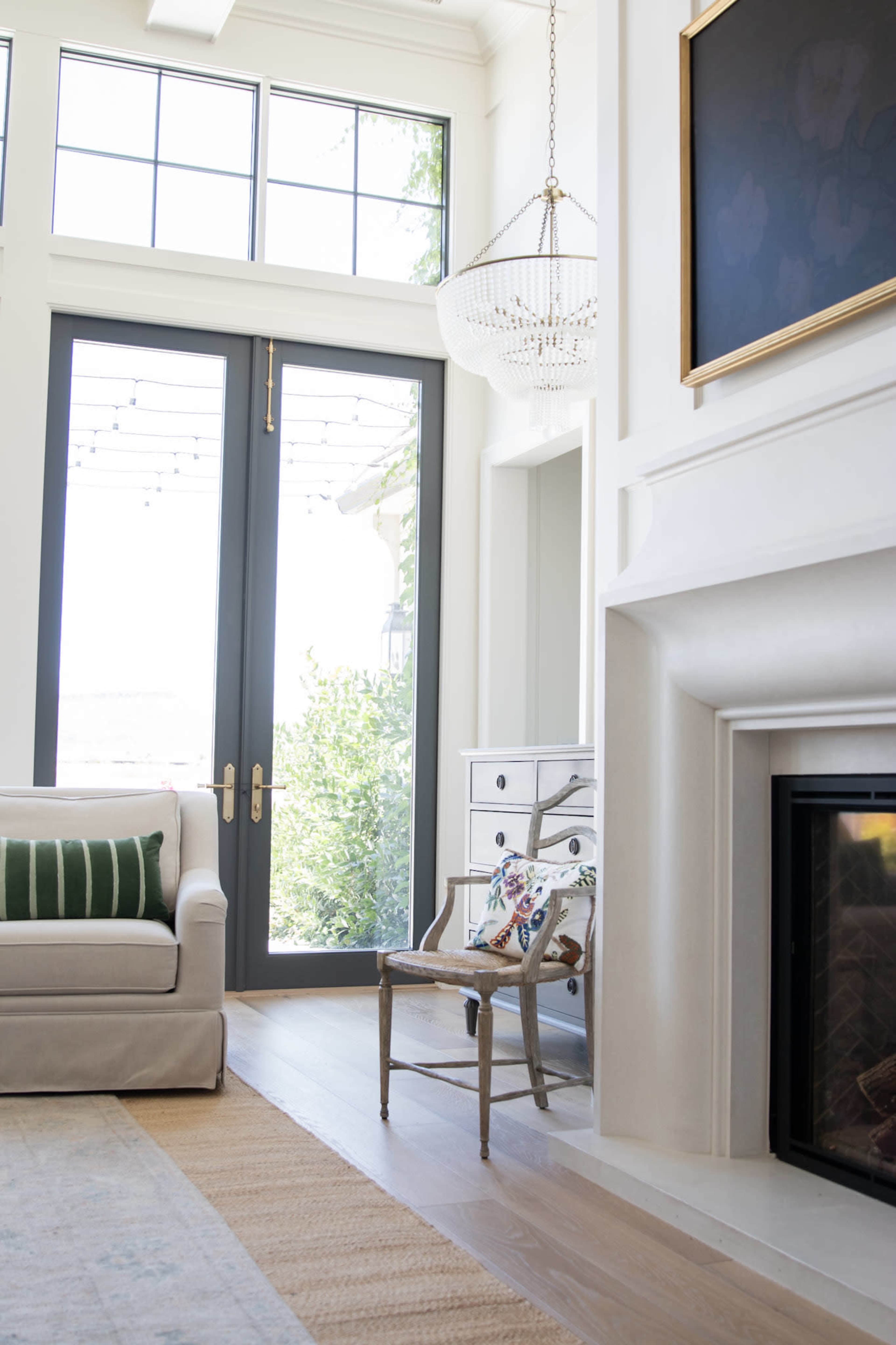 A living room features large windows with a view, a light-colored sofa, a decorative chair, and a fireplace.