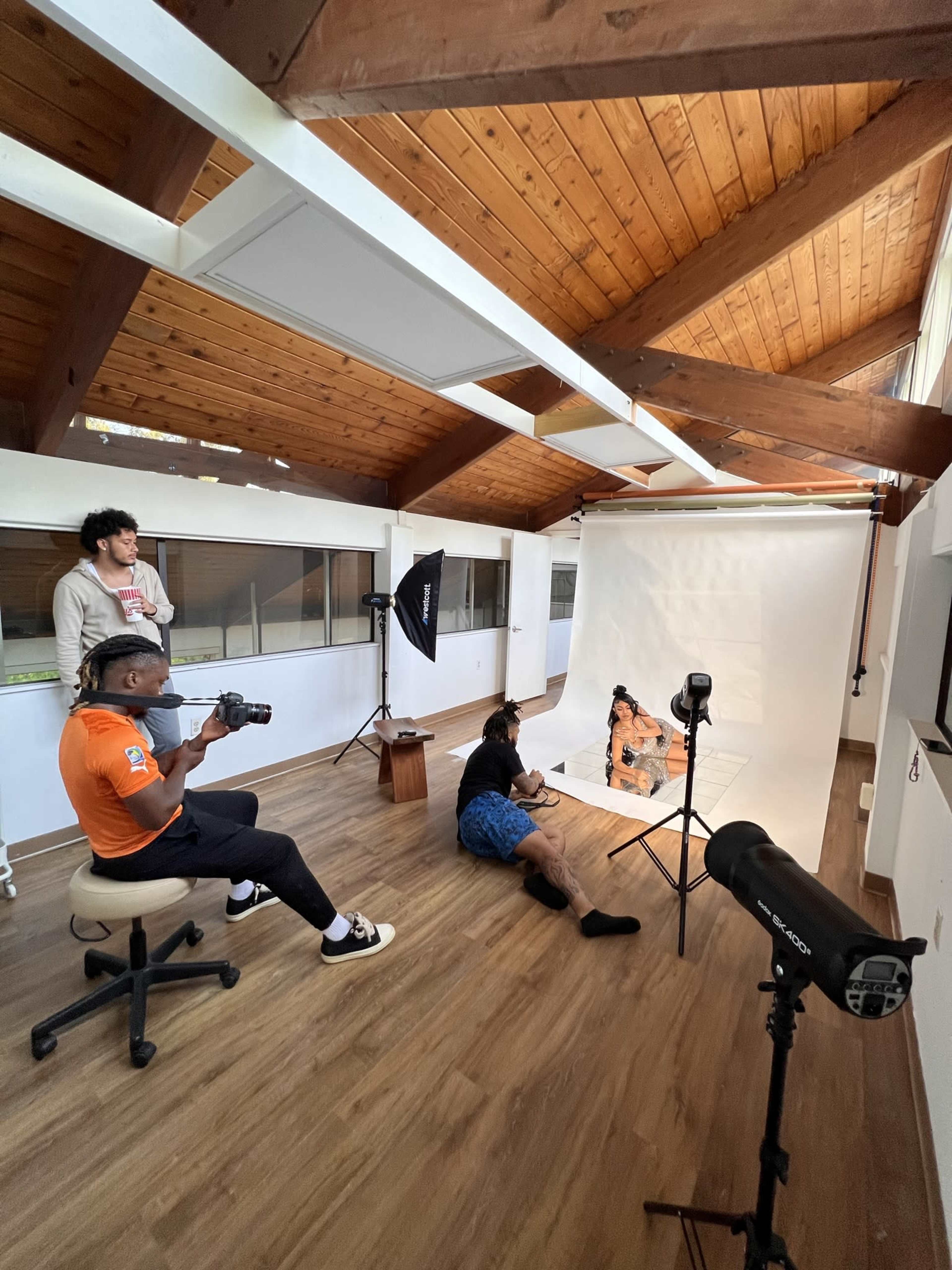 A group of people are participating in a photo shoot inside a well-lit studio with wooden ceilings and a blank backdrop.