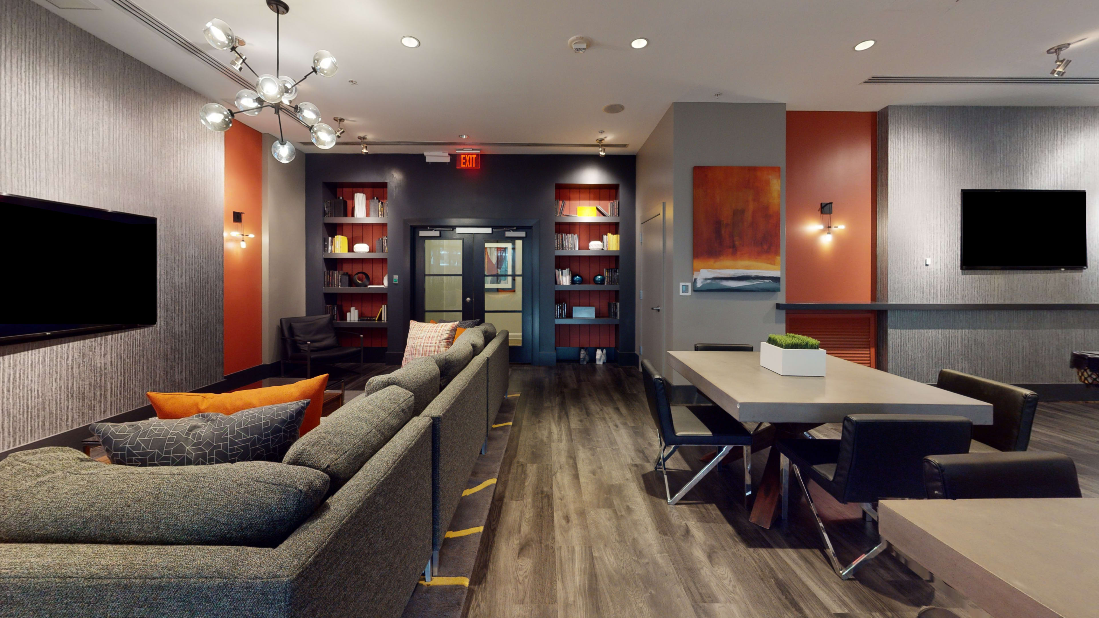 The image shows a modern lounge area featuring a sectional sofa, a dining table, and a bookshelf against a backdrop of textured walls and contrasting colors.