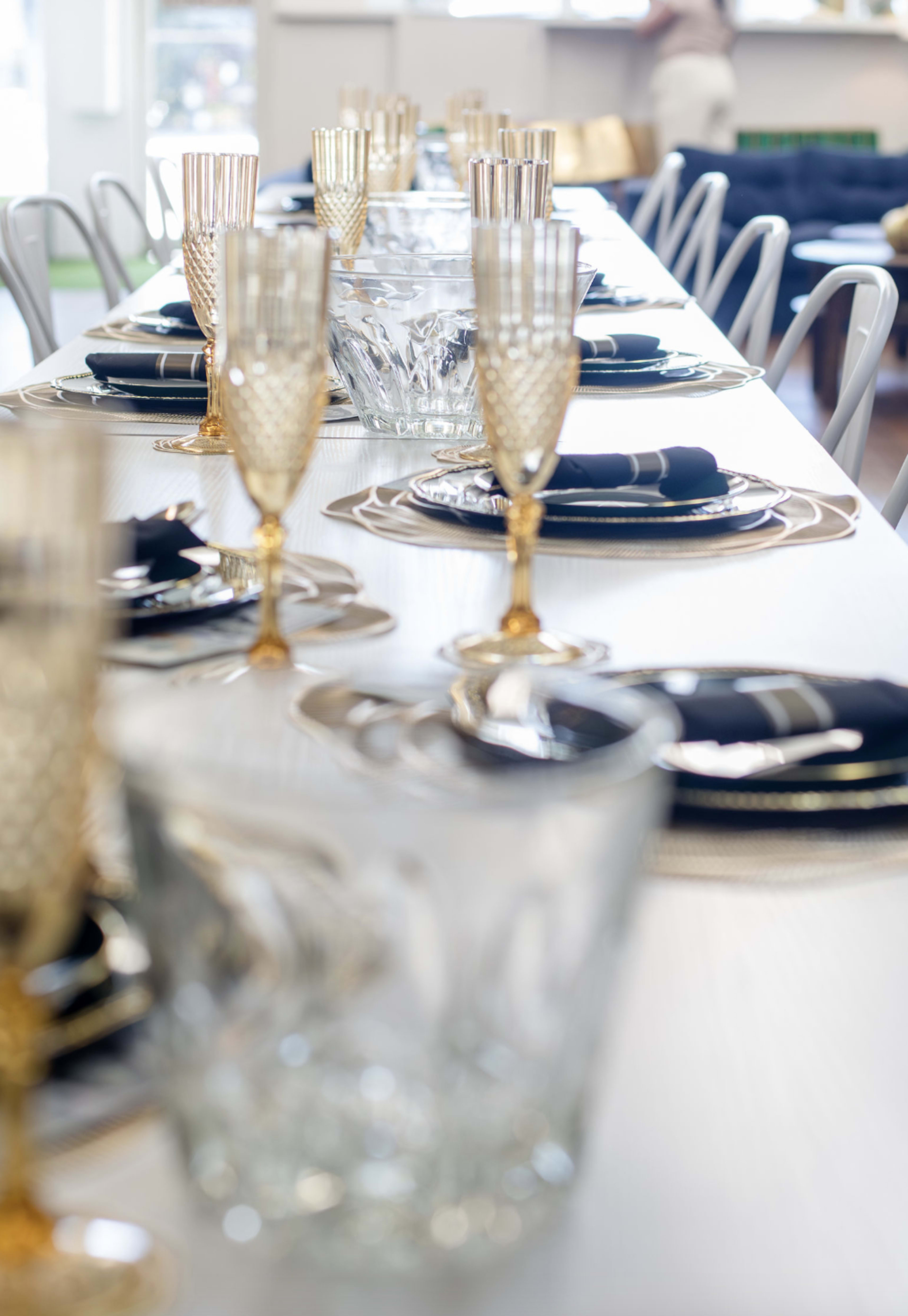 A long dining table is set with elegant glassware, stylish plates, and napkins, arranged for a formal meal.