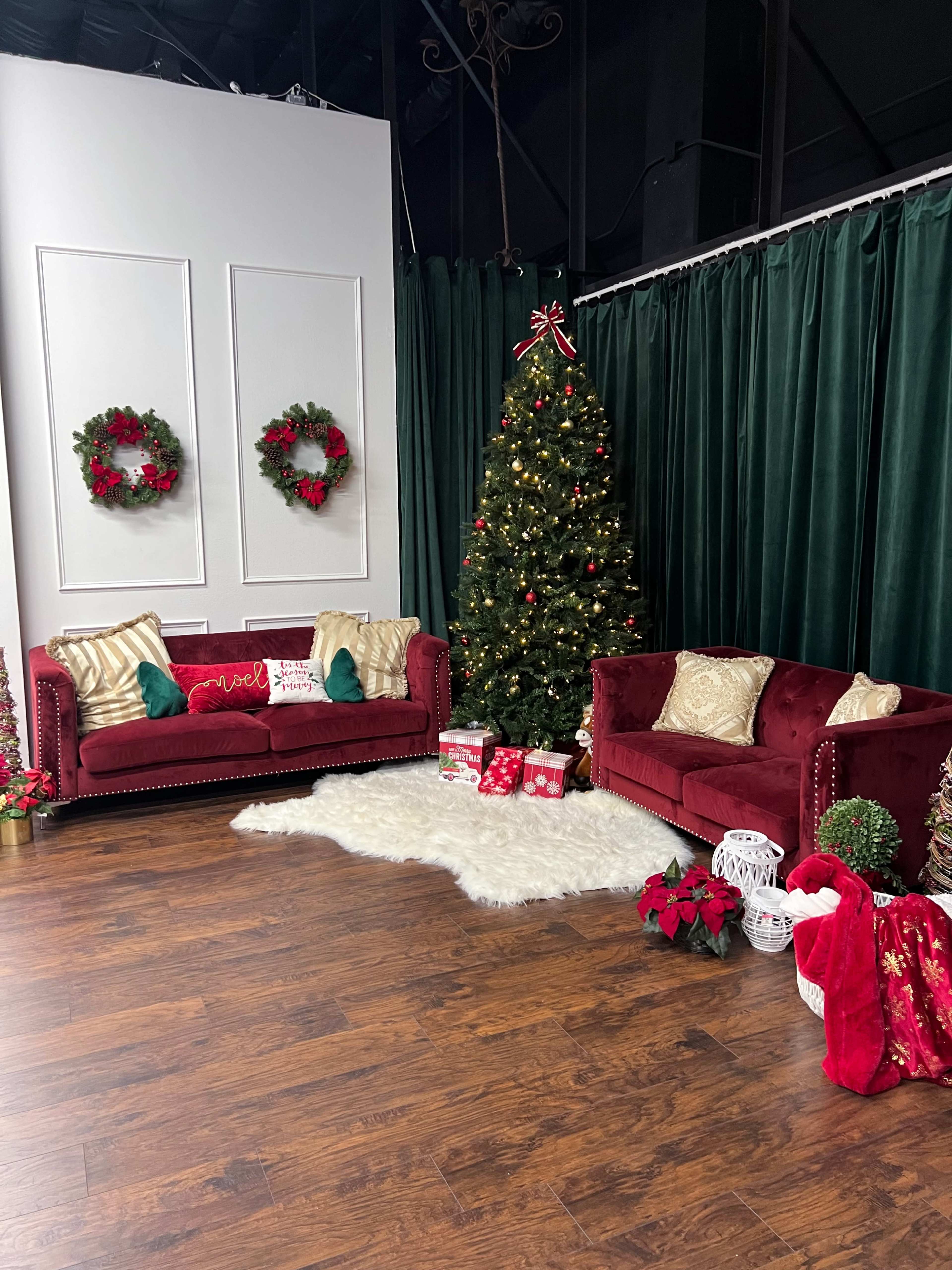 The scene shows a holiday-themed decor area featuring a Christmas tree adorned with lights and ornaments, two red couches with festive pillows, and decorative elements like wreaths and poinsettias.