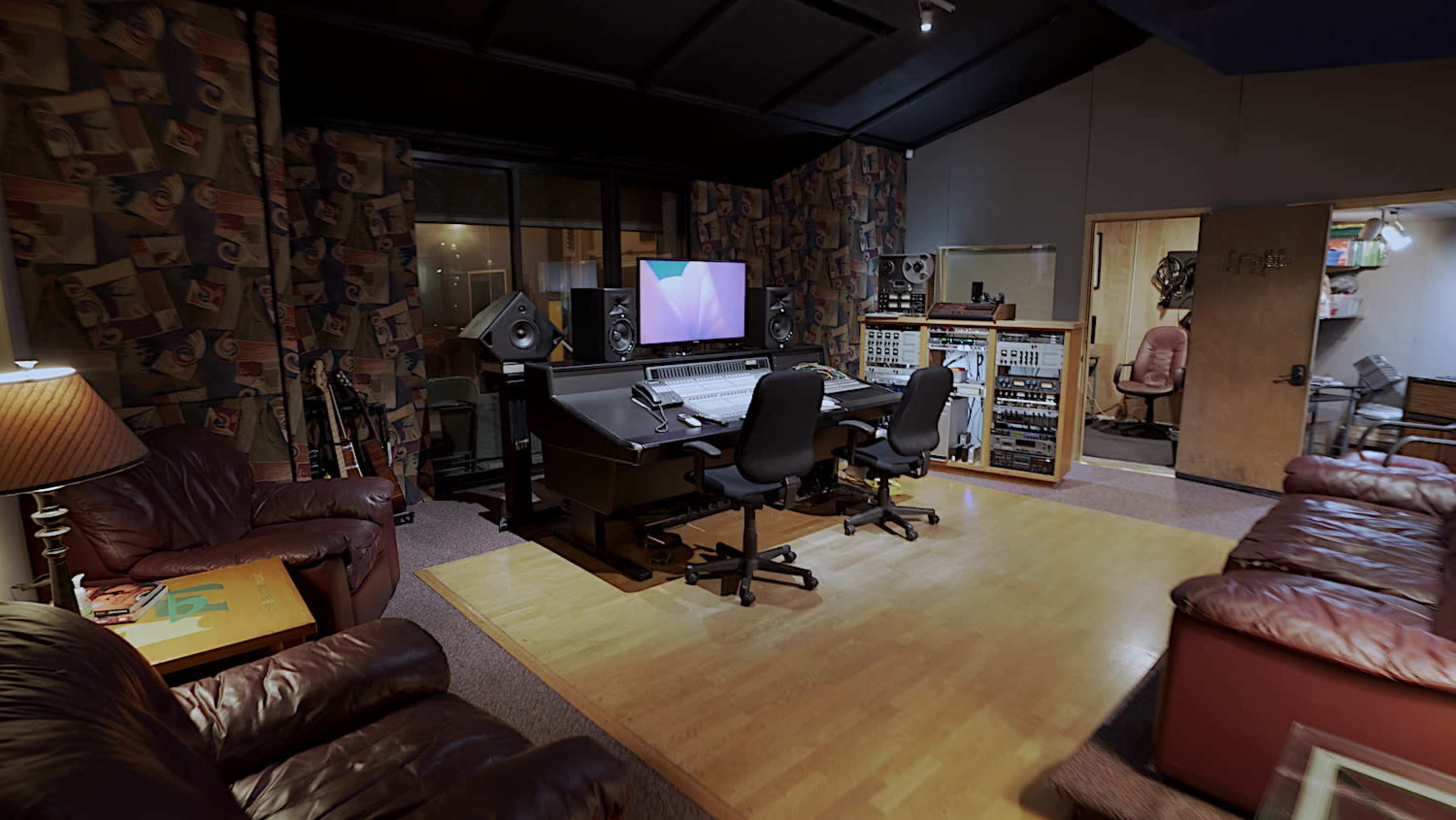 A well-equipped music recording studio featuring a mixing desk, monitors, and comfortable seating areas.