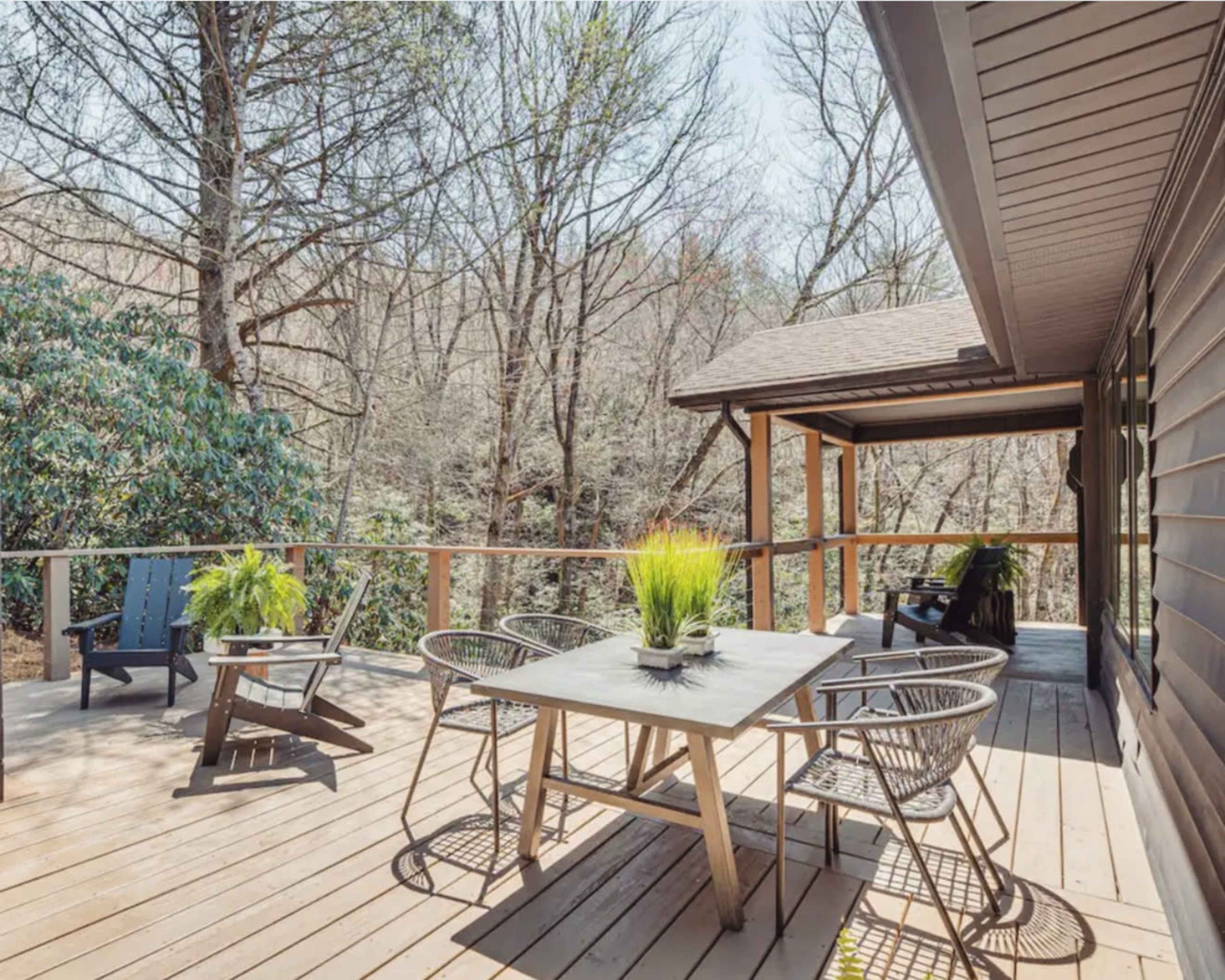 A wooden deck features a table and chairs surrounded by trees on a sunny day.