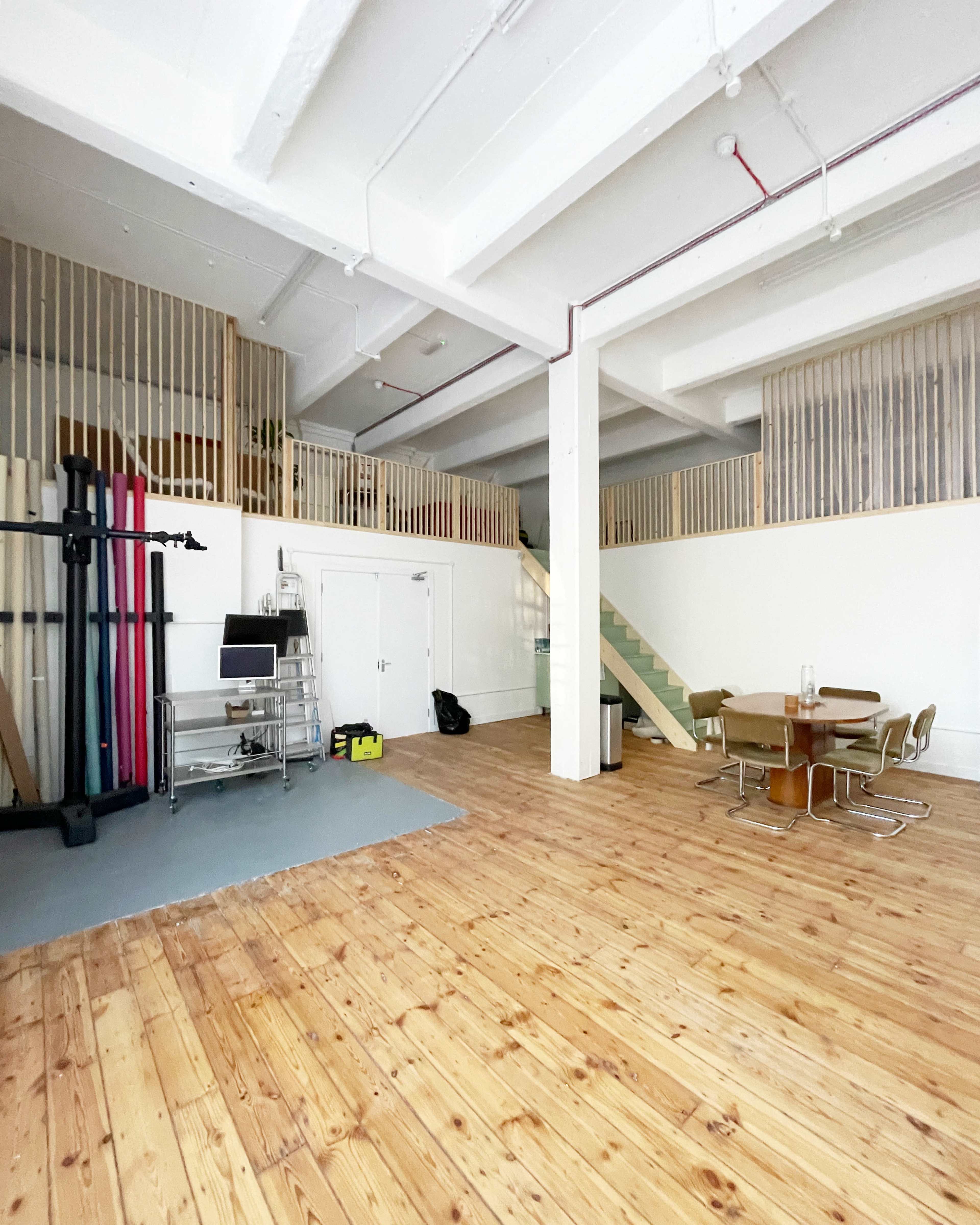 A spacious interior with wooden flooring, featuring a table and chairs, a staircase leading to an upper level, and exercise equipment against one wall.