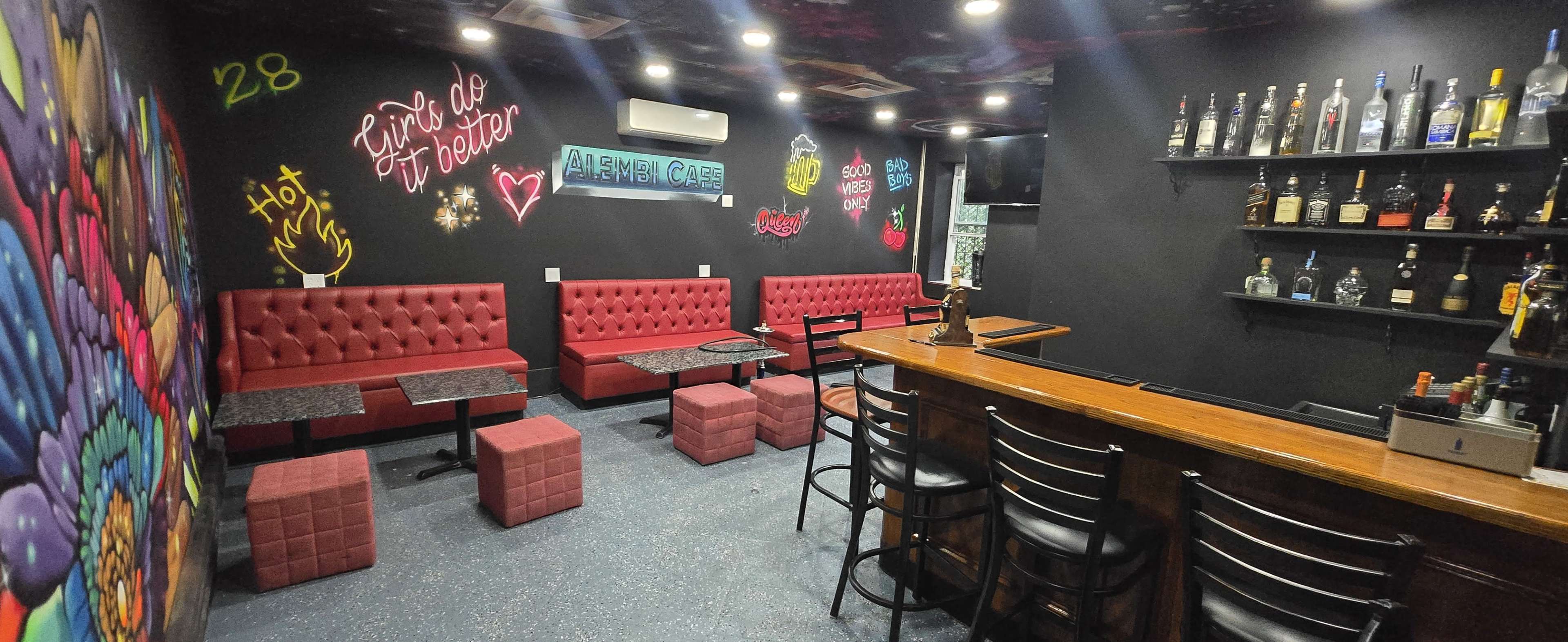 The image shows a dimly lit lounge with red upholstered seating, a wooden bar, and a colorful graffiti wall.