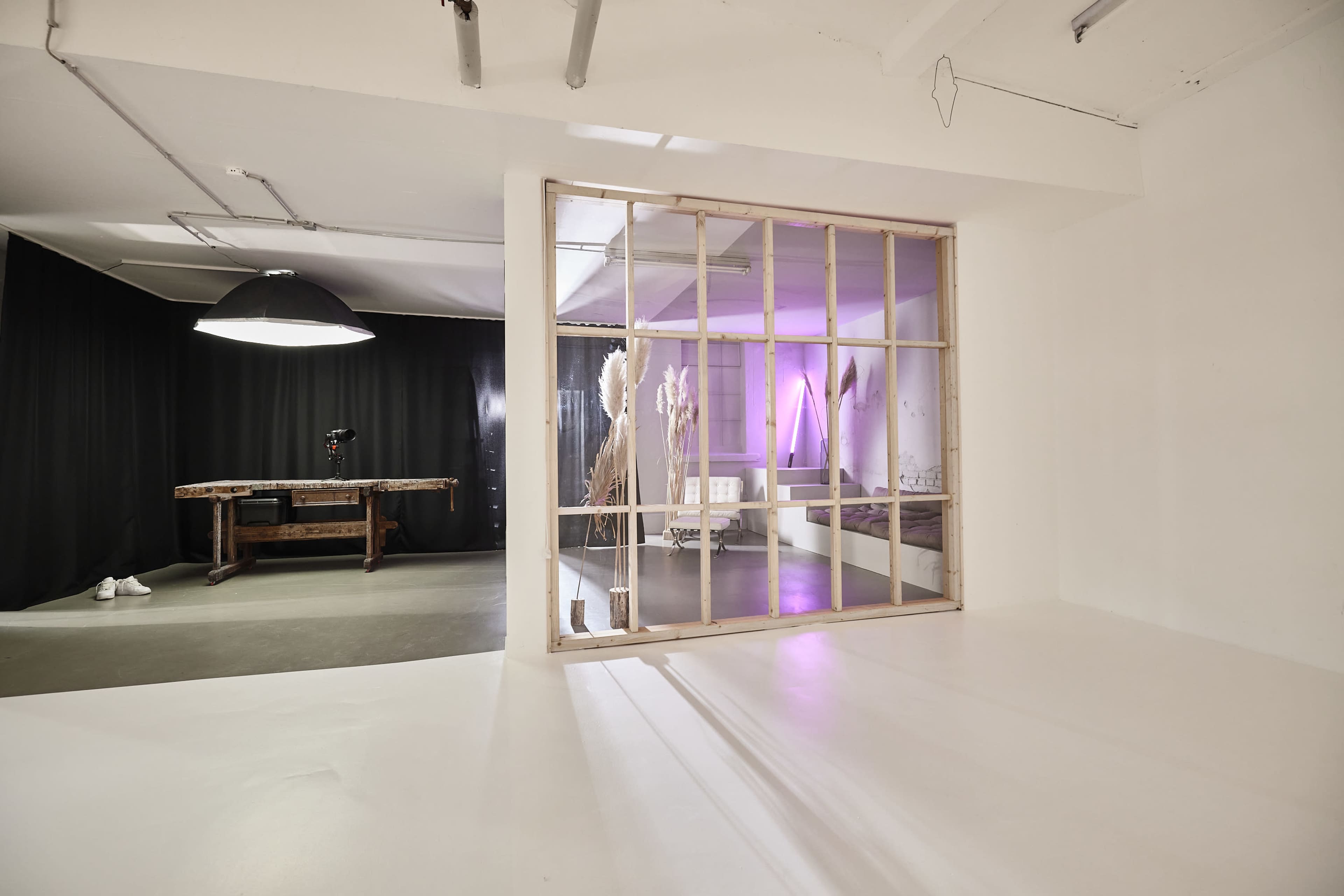 The image shows a spacious, modern interior with a wooden frame separating two areas, one featuring a dark backdrop and a light fixture, and the other illuminated with colored lights.