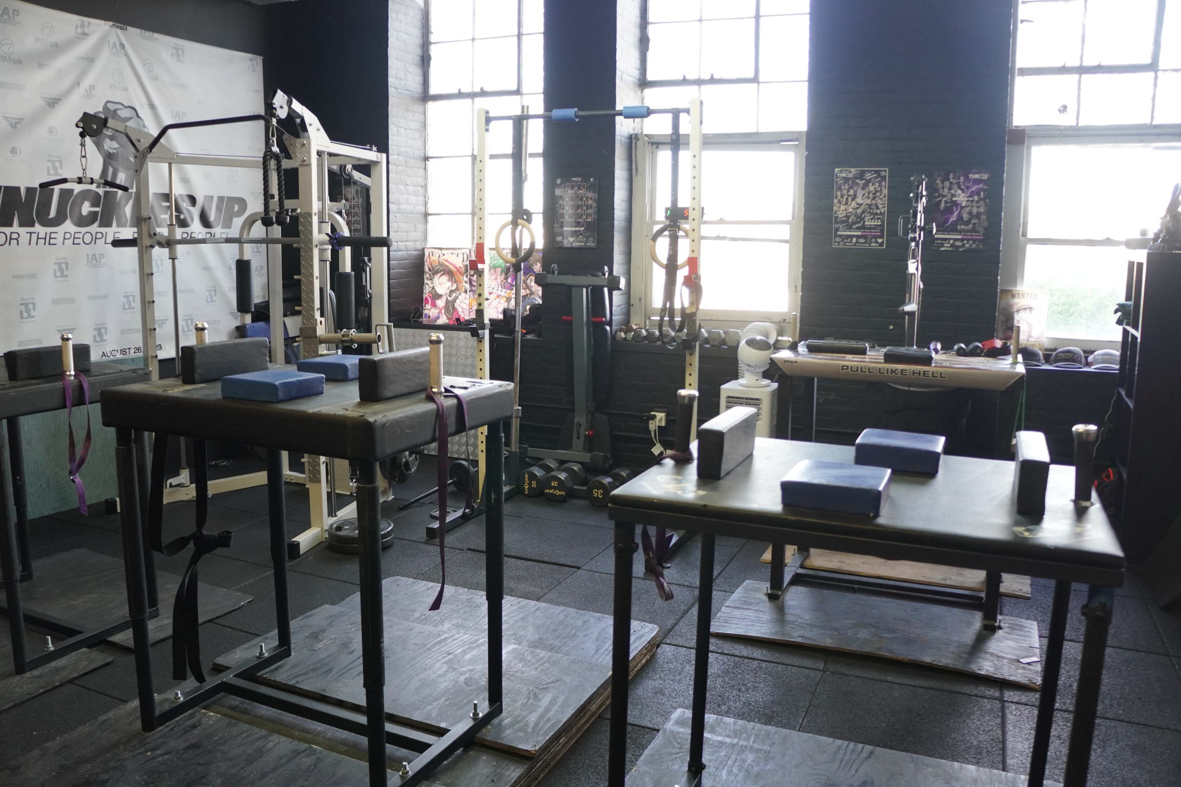 The image shows a gym interior with various workout stations, including parallel bars and weightlifting equipment, surrounded by large windows.