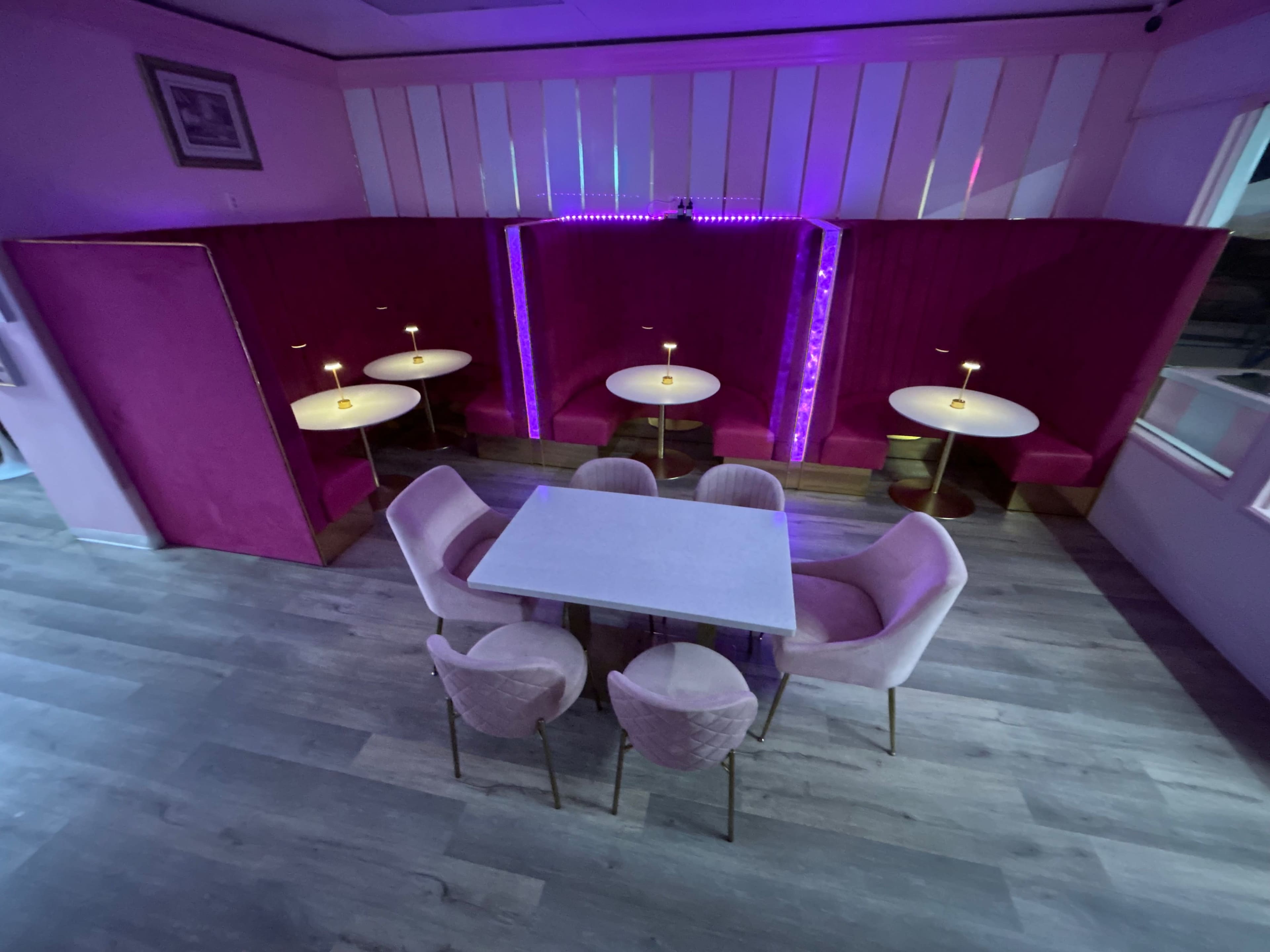 A restaurant interior with purple upholstered booths and small round tables arranged around a central square table.