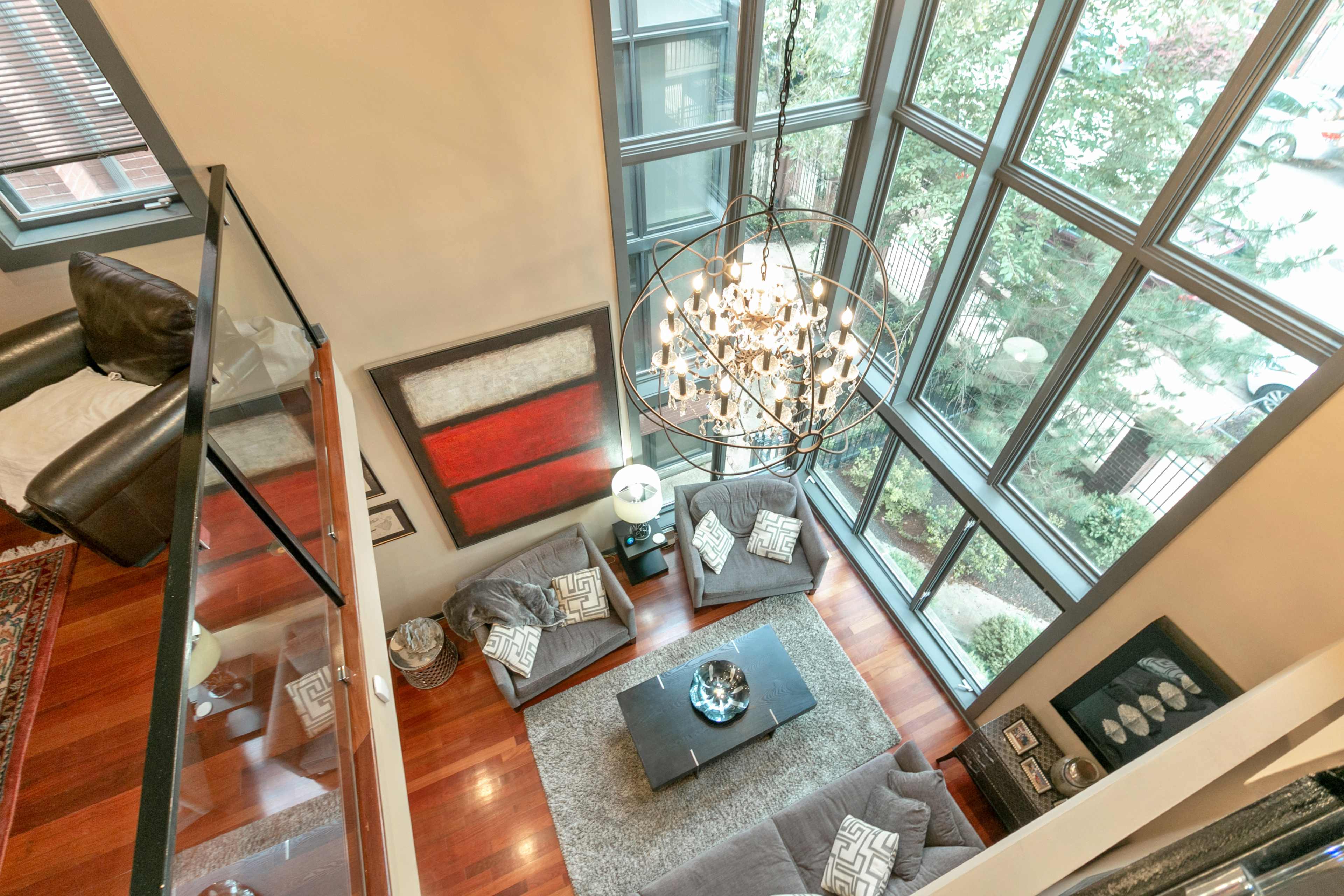 A spacious living room with large windows, a modern chandelier, and a staircase leading to an upper level.