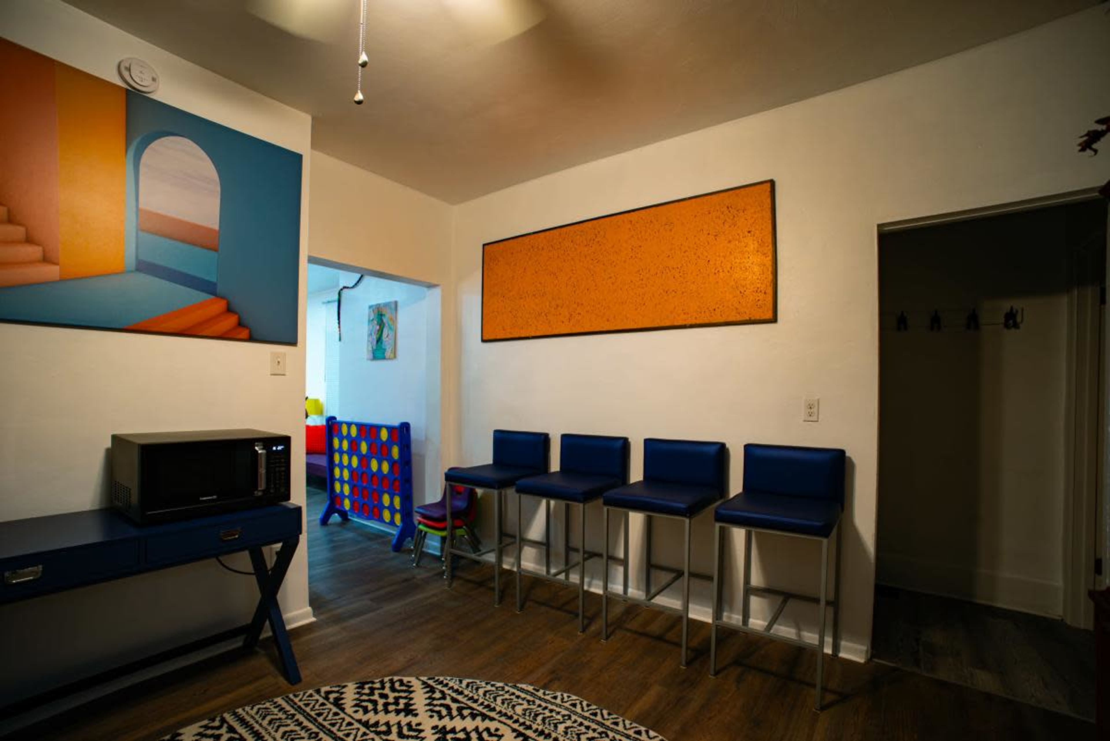 The image shows a modern room with a blue-painted bar area, four blue stools, a black microwave, and an orange wall art piece.