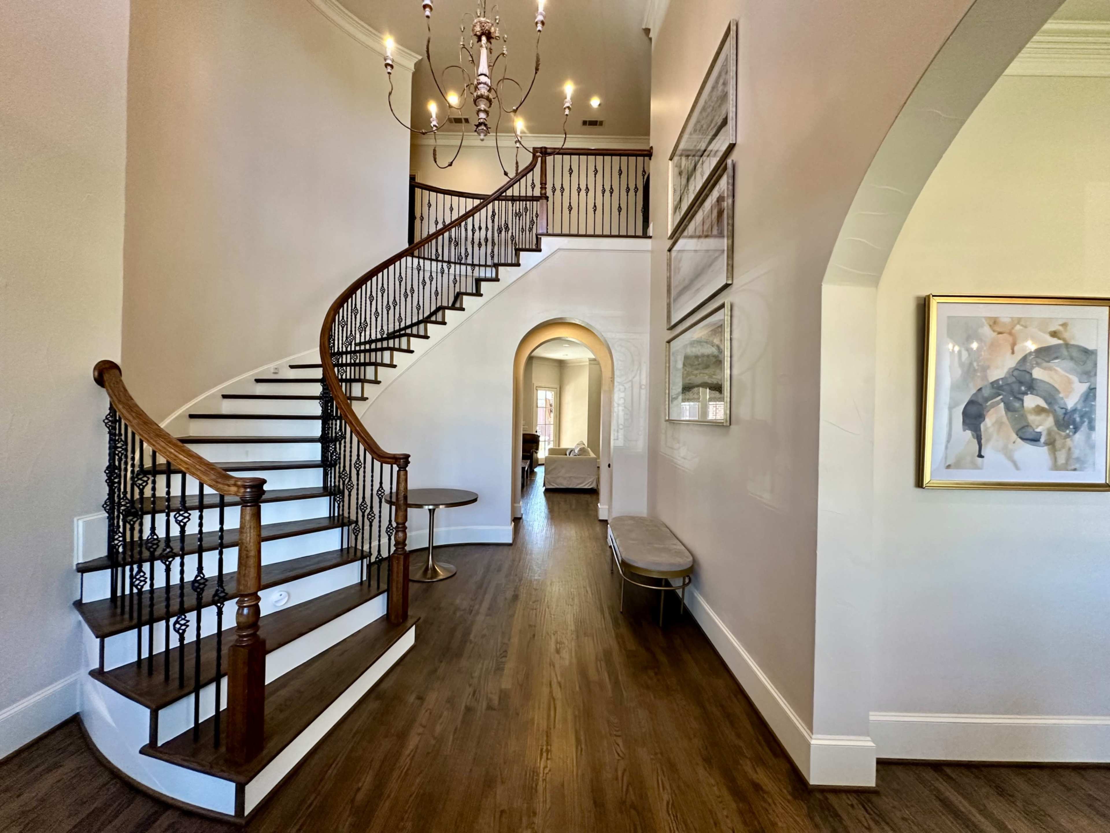 A staircase with a curved wooden railing leads to an upper level in a spacious, well-lit hallway.
