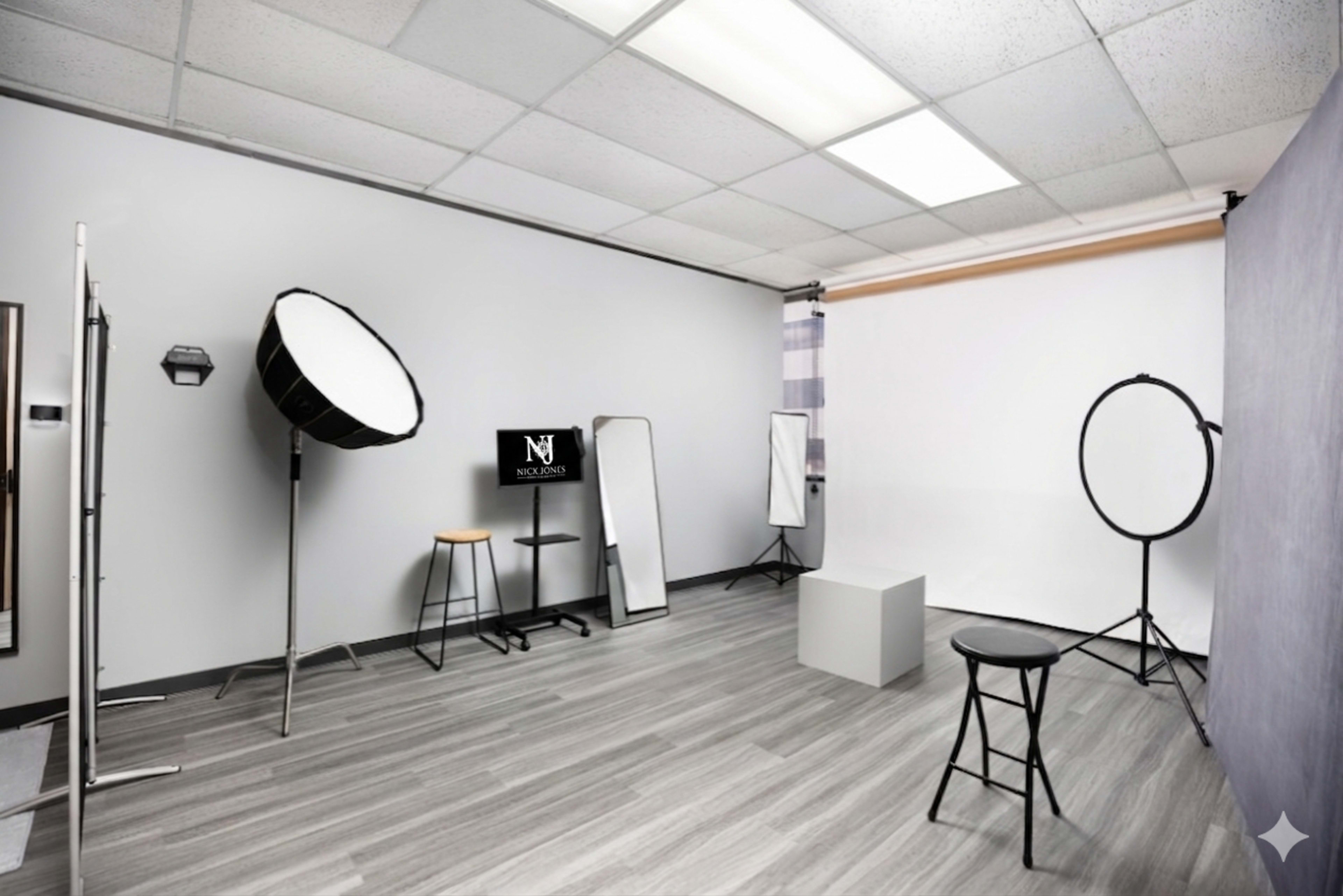 The image shows a photography studio featuring lighting equipment, mirrors, and a blank backdrop with a stool and a small platform in the center.