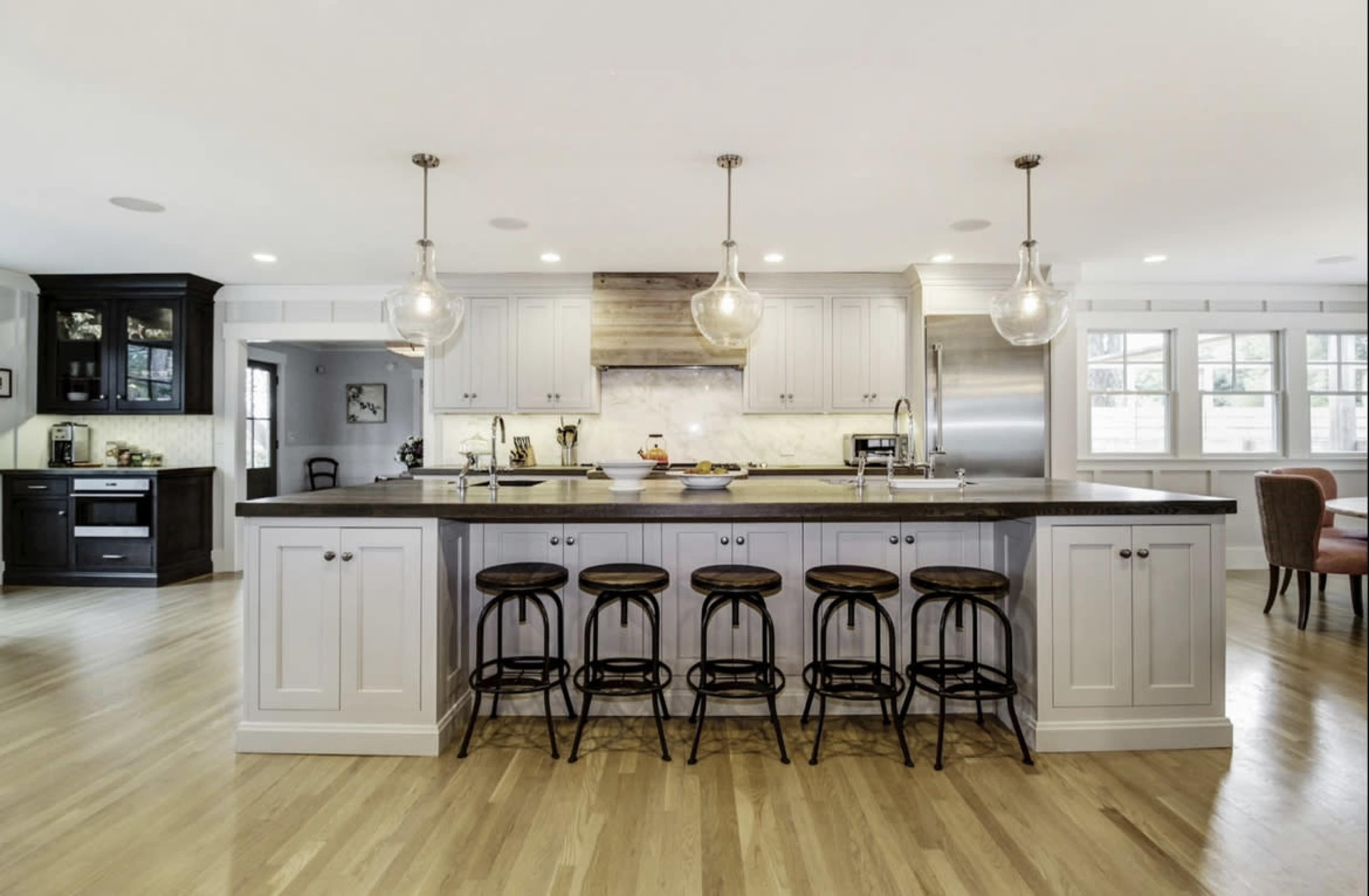 A modern kitchen featuring a central island with six bar stools, pendant lighting, and stainless steel appliances.