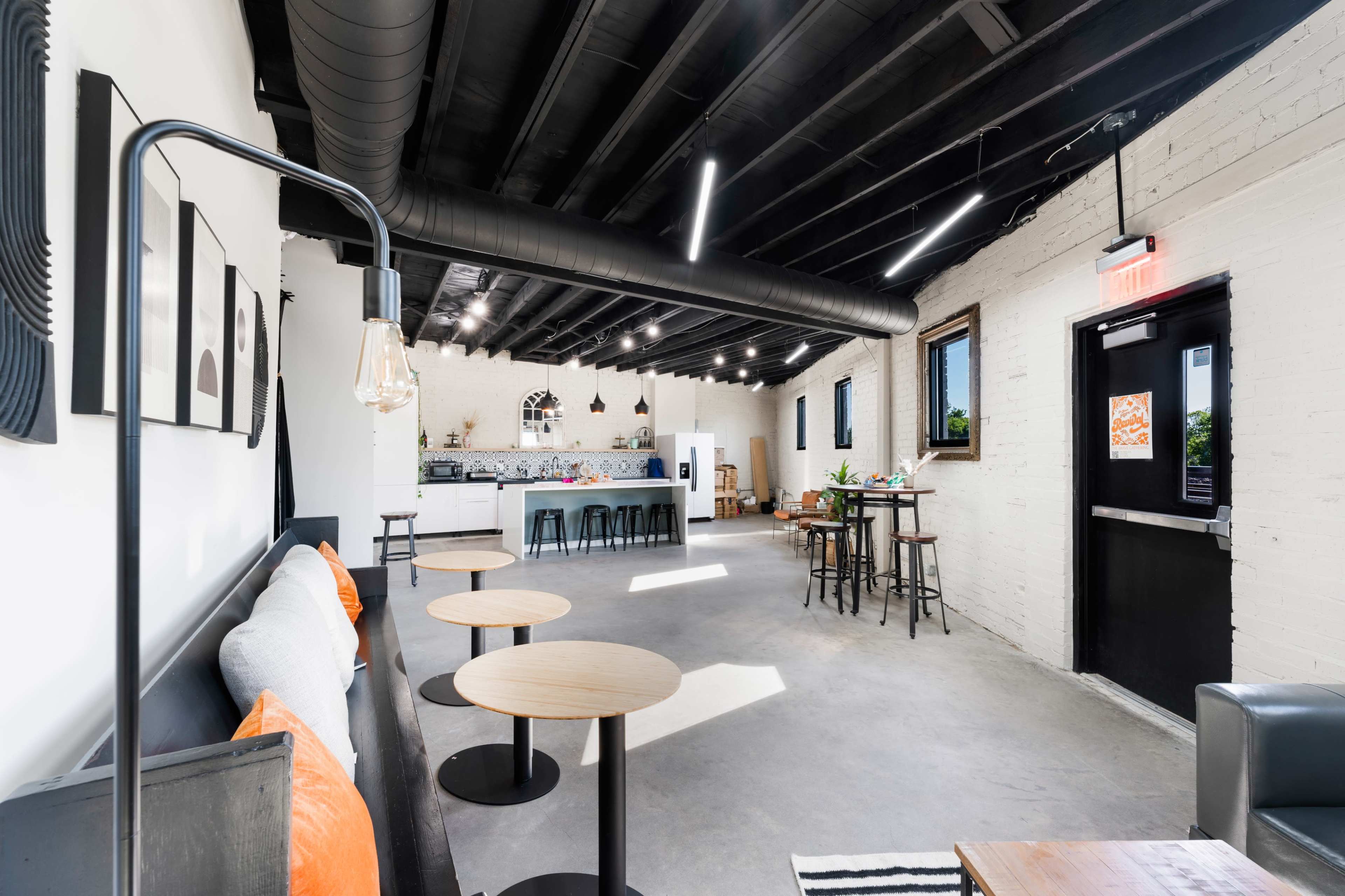 The image shows a modern, minimalistic interior of a café with light-colored walls, several small tables, and a counter in the background.