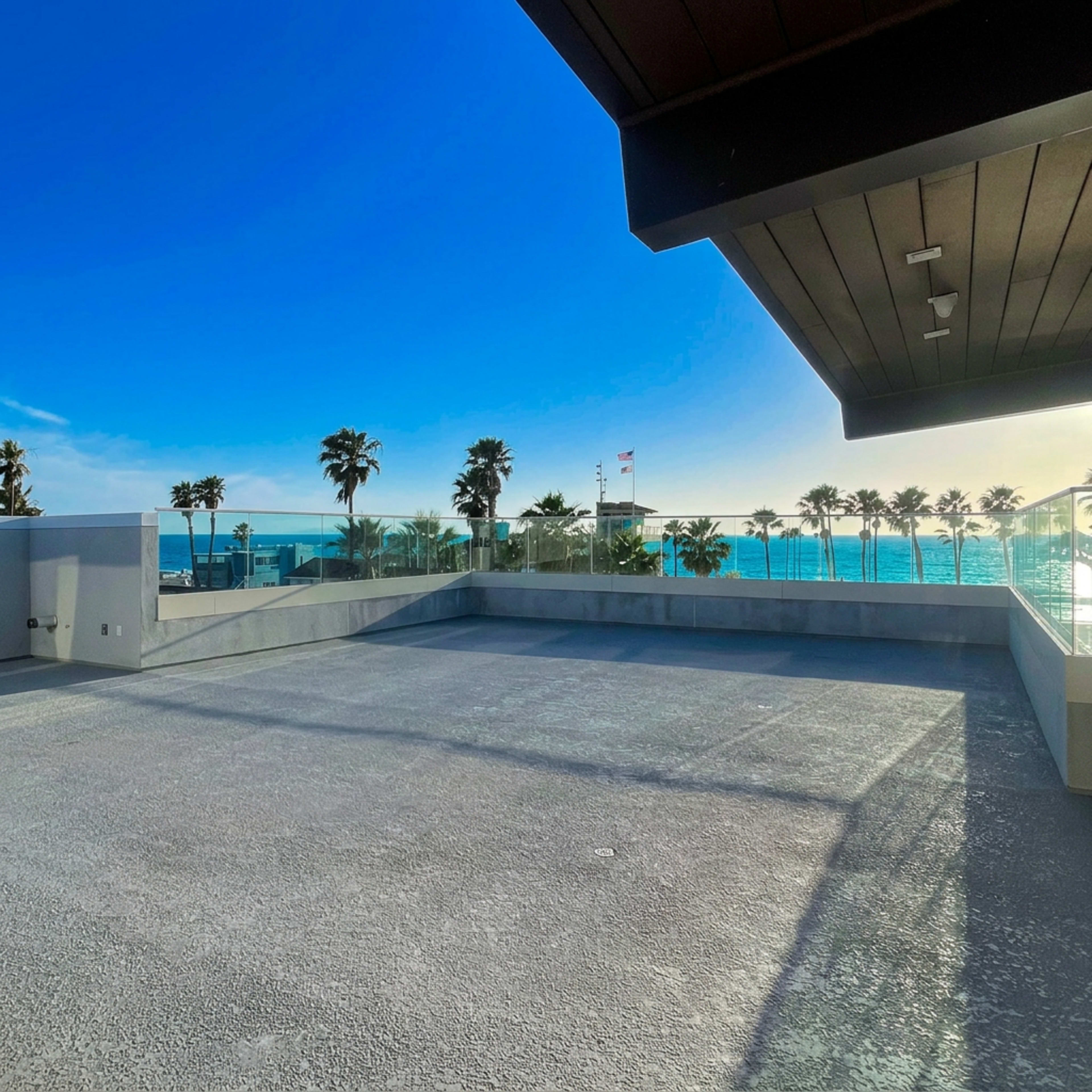 The image shows a spacious rooftop terrace with a clear view of the ocean and palm trees under a blue sky.