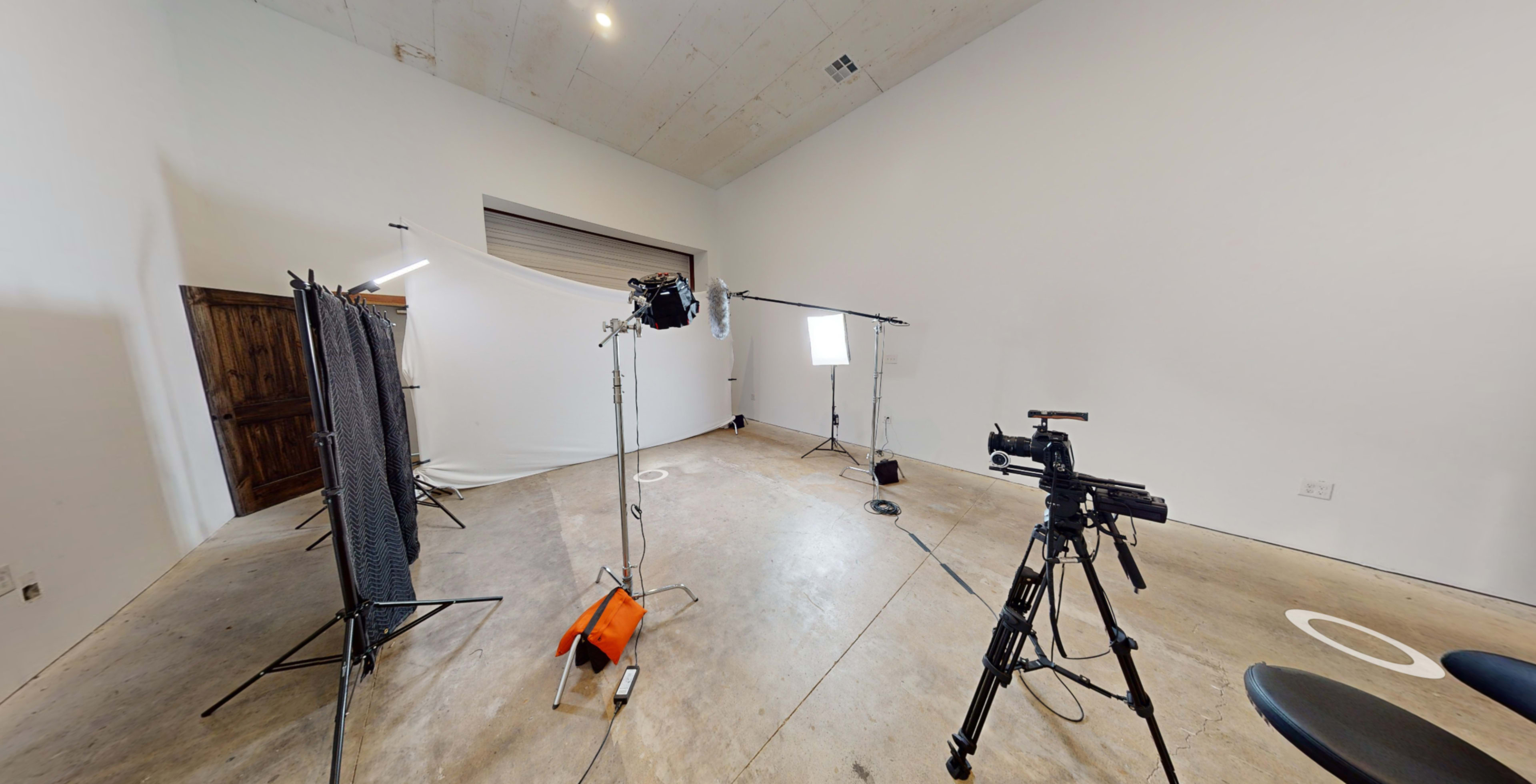 A sparse studio with various lighting equipment and cameras set up on a concrete floor.