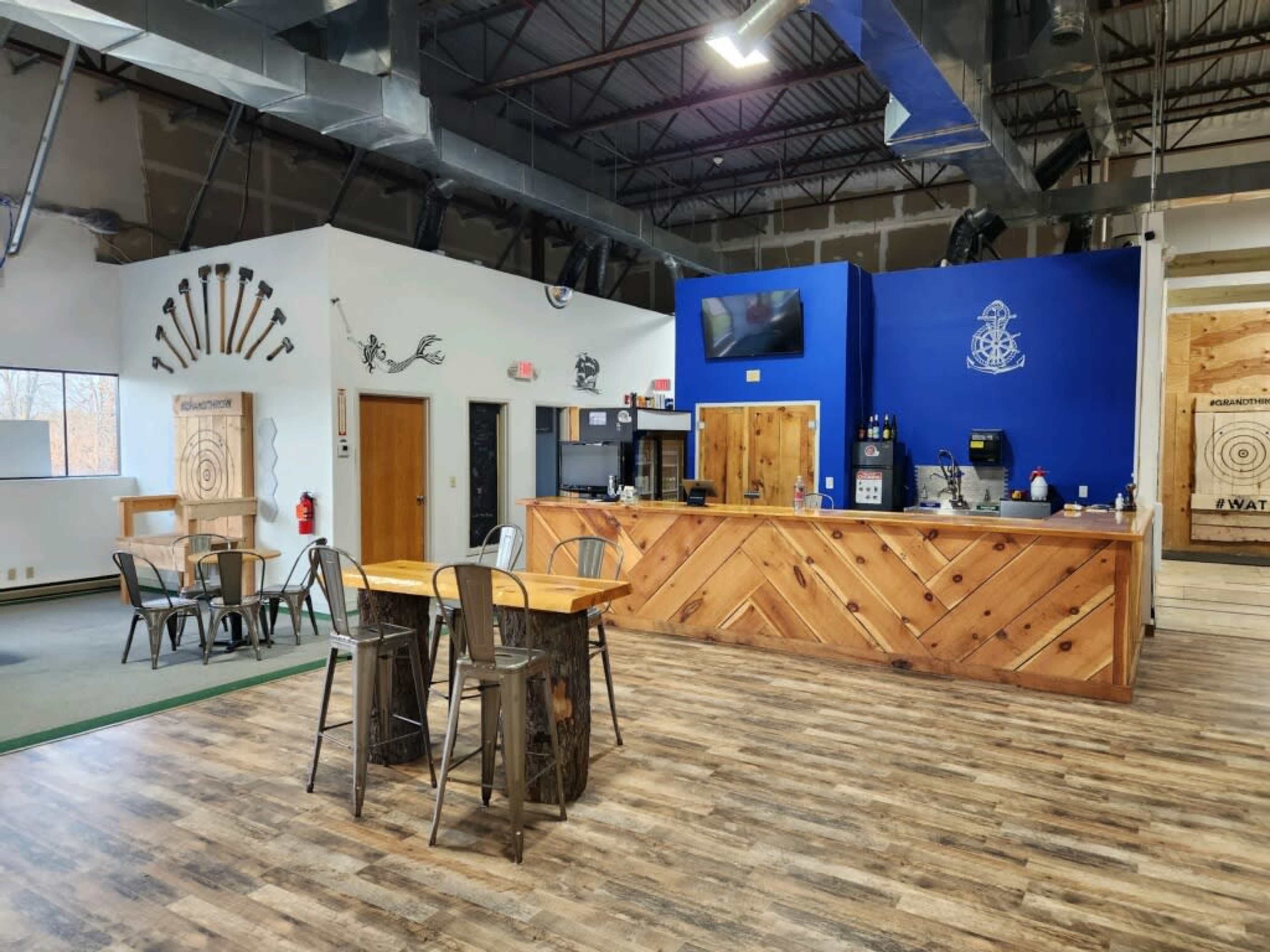 A spacious interior of a venue featuring a wooden reception counter, seating area with metal chairs, and target boards on the walls.