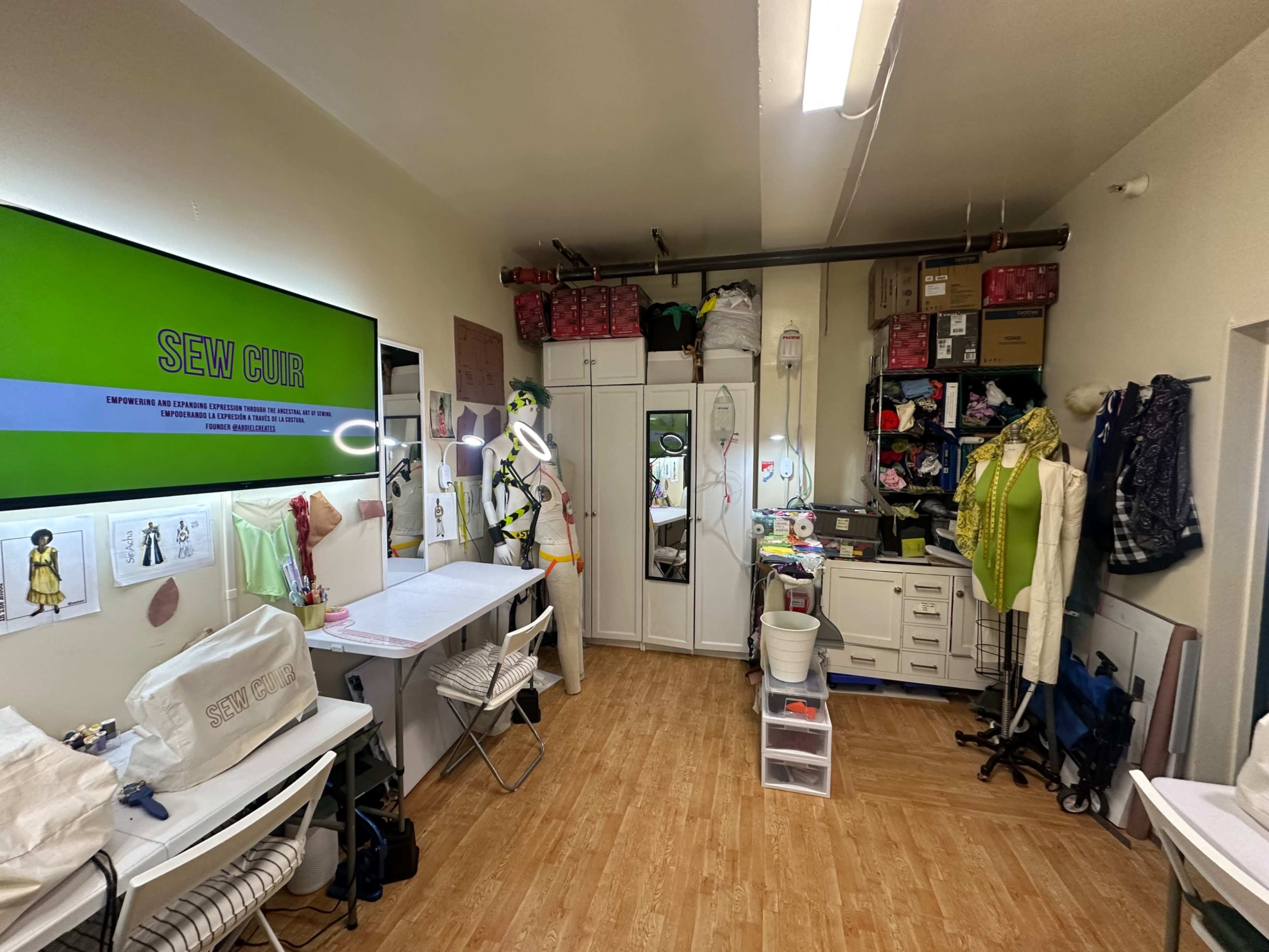 The image shows a sewing studio filled with various fabrics, tools, and organized storage, featuring multiple workstations and a mannequin.