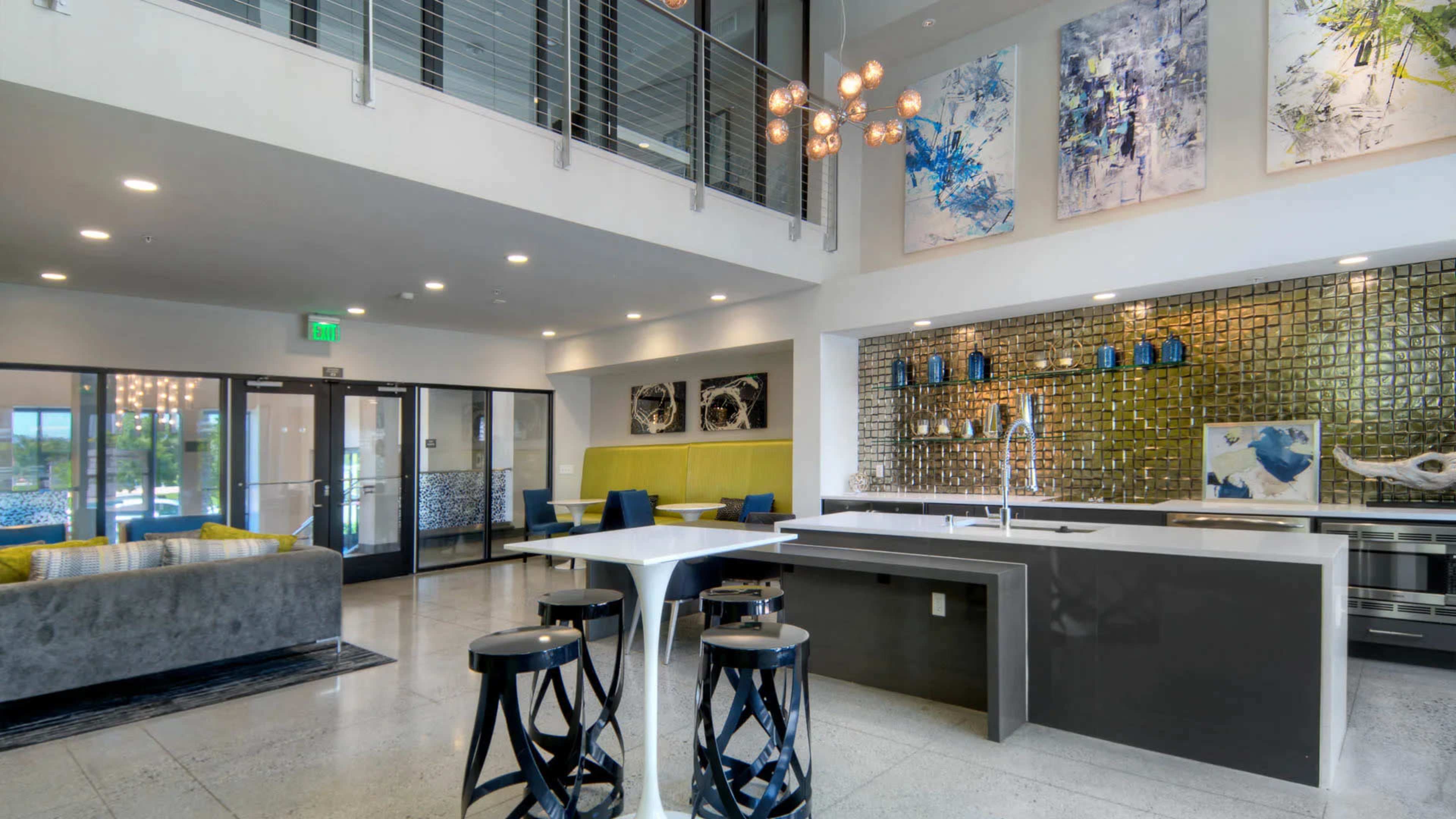 A modern lobby area with a kitchen island, seating areas, and abstract art on the walls, featuring a mix of textures and colors.