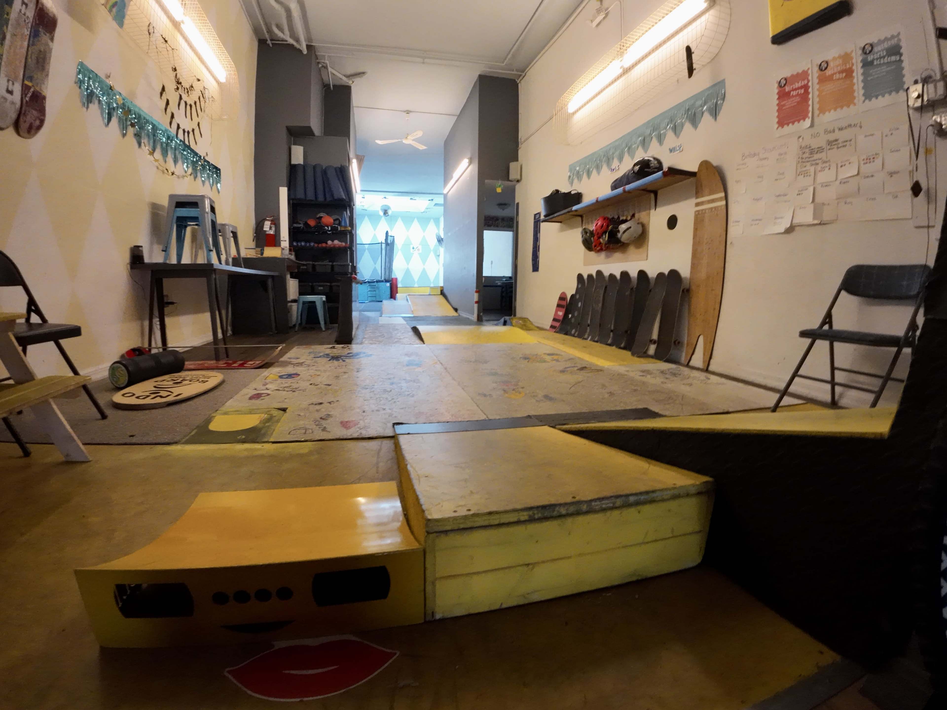 The image shows an indoor skateboarding area with a ramp and several skateboards resting on the wall.